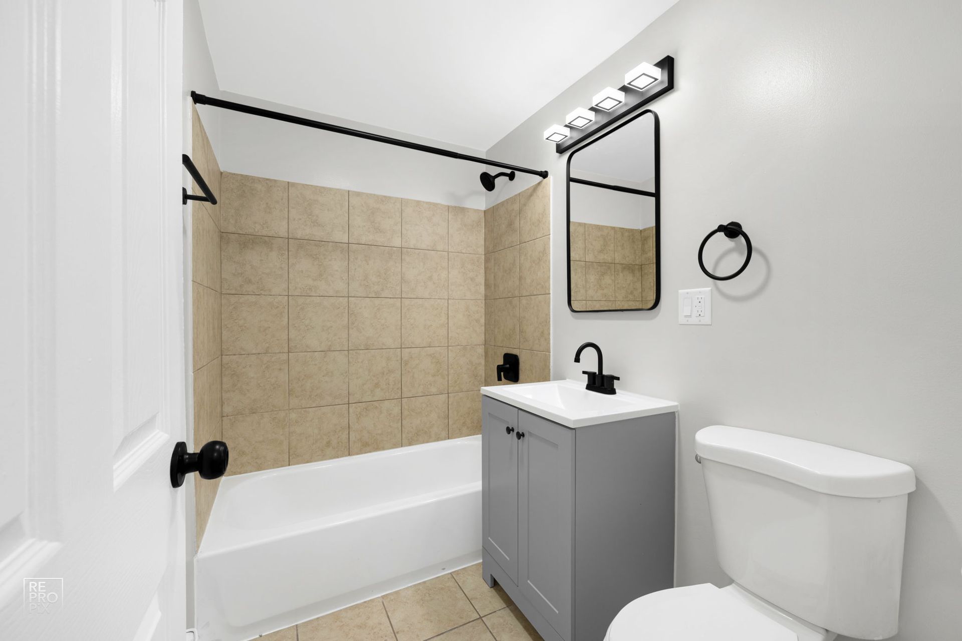 Bathroom with gray vanity, white toilet, and beige tiled shower.