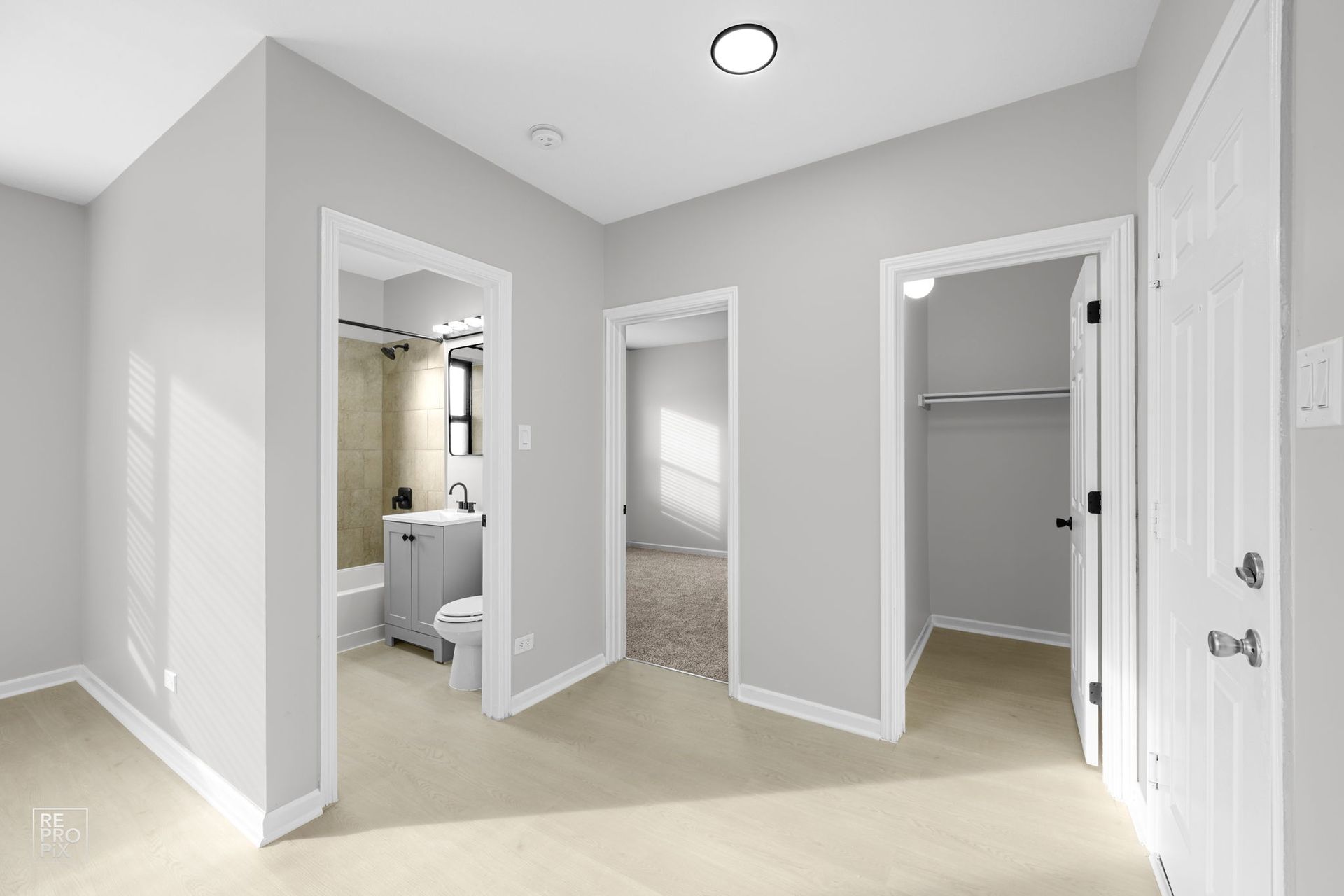 Empty room with three doorways: bathroom, closet, and another room. Light tan carpet and gray walls.