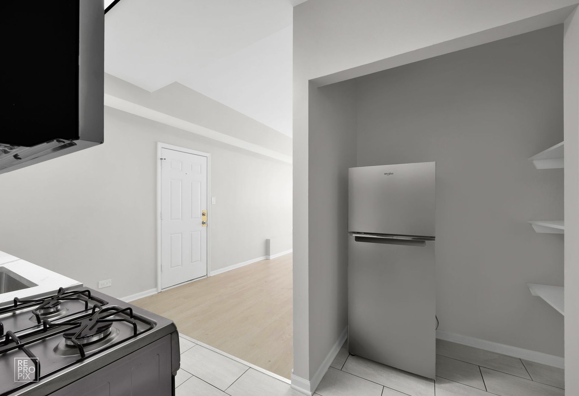 Kitchen with stove, refrigerator, door to hallway, and pantry with shelves.