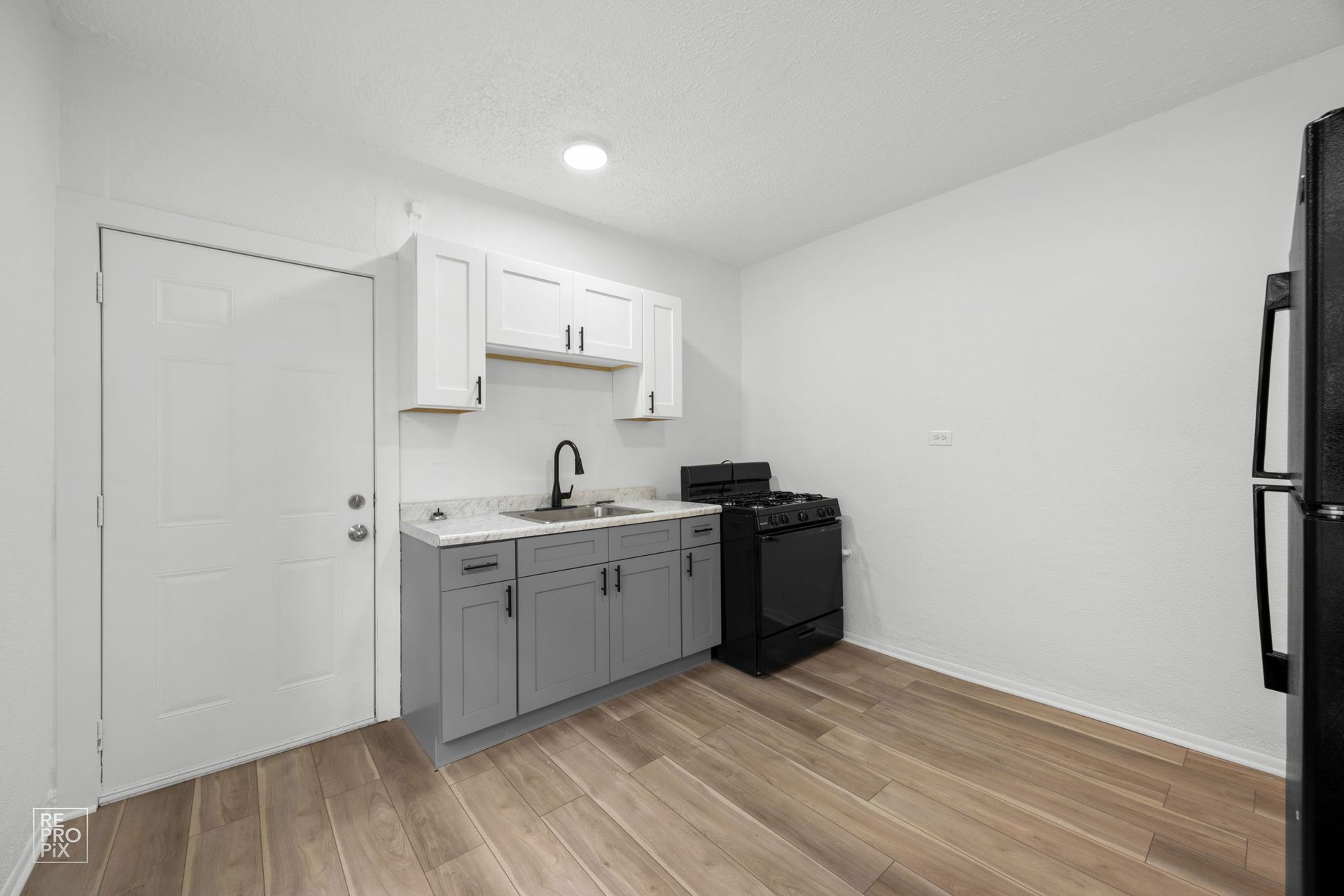 Small kitchen with gray and white cabinets, black appliances, and wood-look flooring.