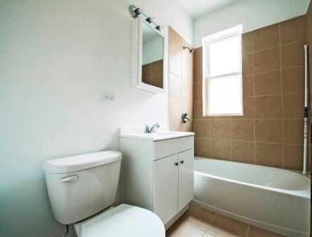 Bathroom with white toilet, vanity, and bathtub with brown tile surround.