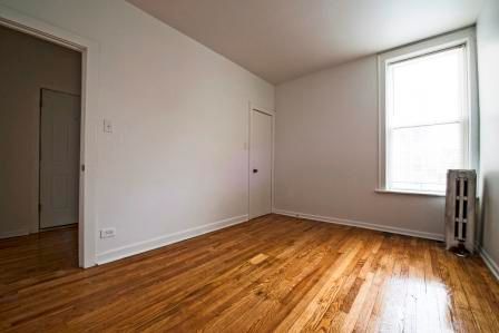 Empty room with hardwood floors, white walls, and a window.