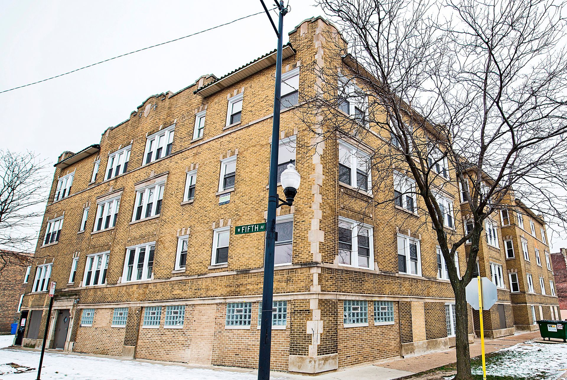 Multi-story brick apartment building on a snowy corner with a street sign.