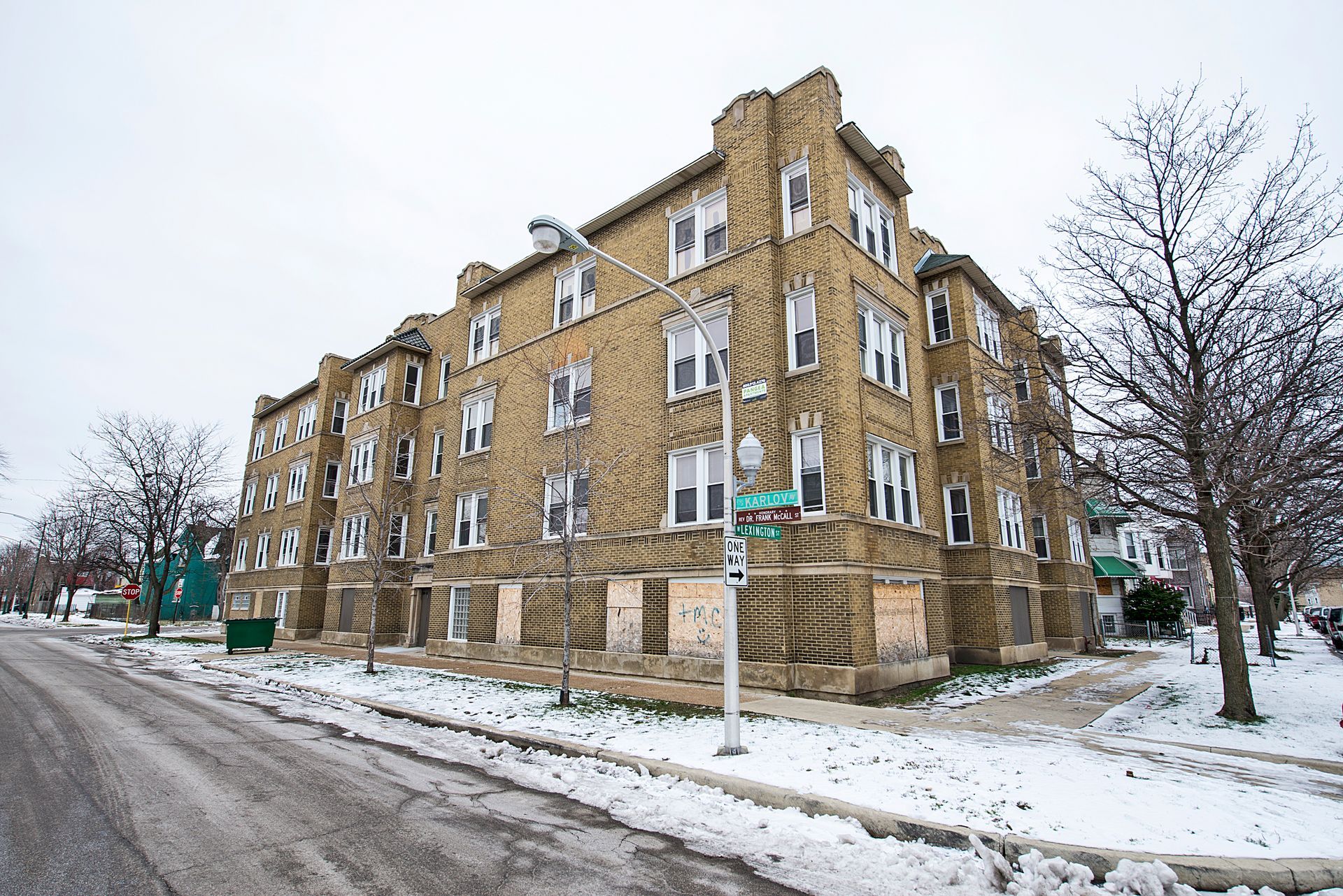 Multi-story tan brick building with boarded-up windows, corner lot, snowy street.
