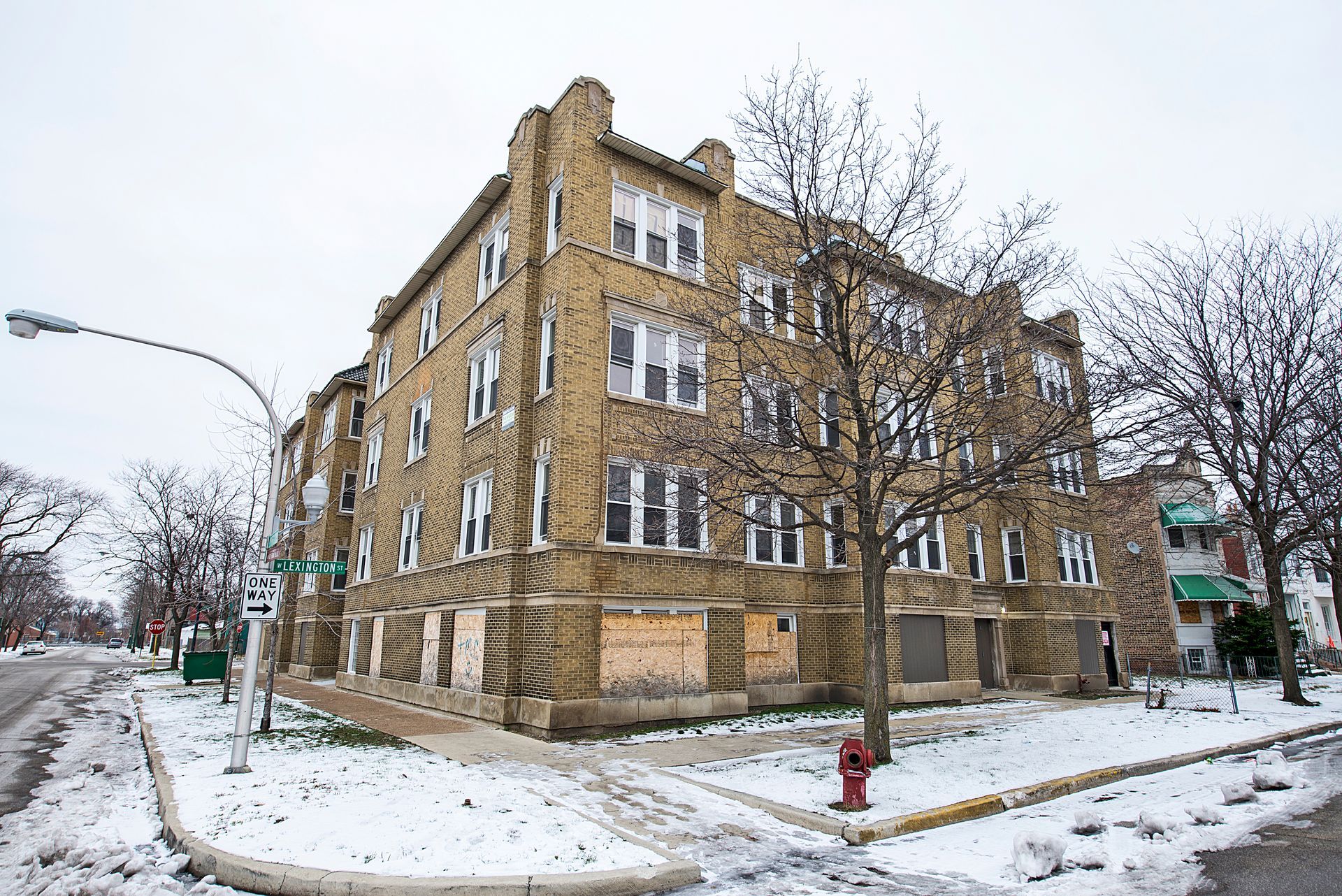 A three-story brick apartment building on a snowy corner lot, boarded up windows.