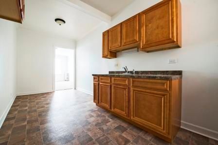 Empty kitchen with wood cabinets, countertop, and patterned floor. White walls, open doorway.