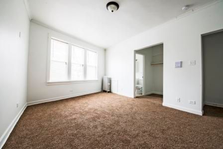 Empty room with brown carpet, window, and doorway leading to bathroom.