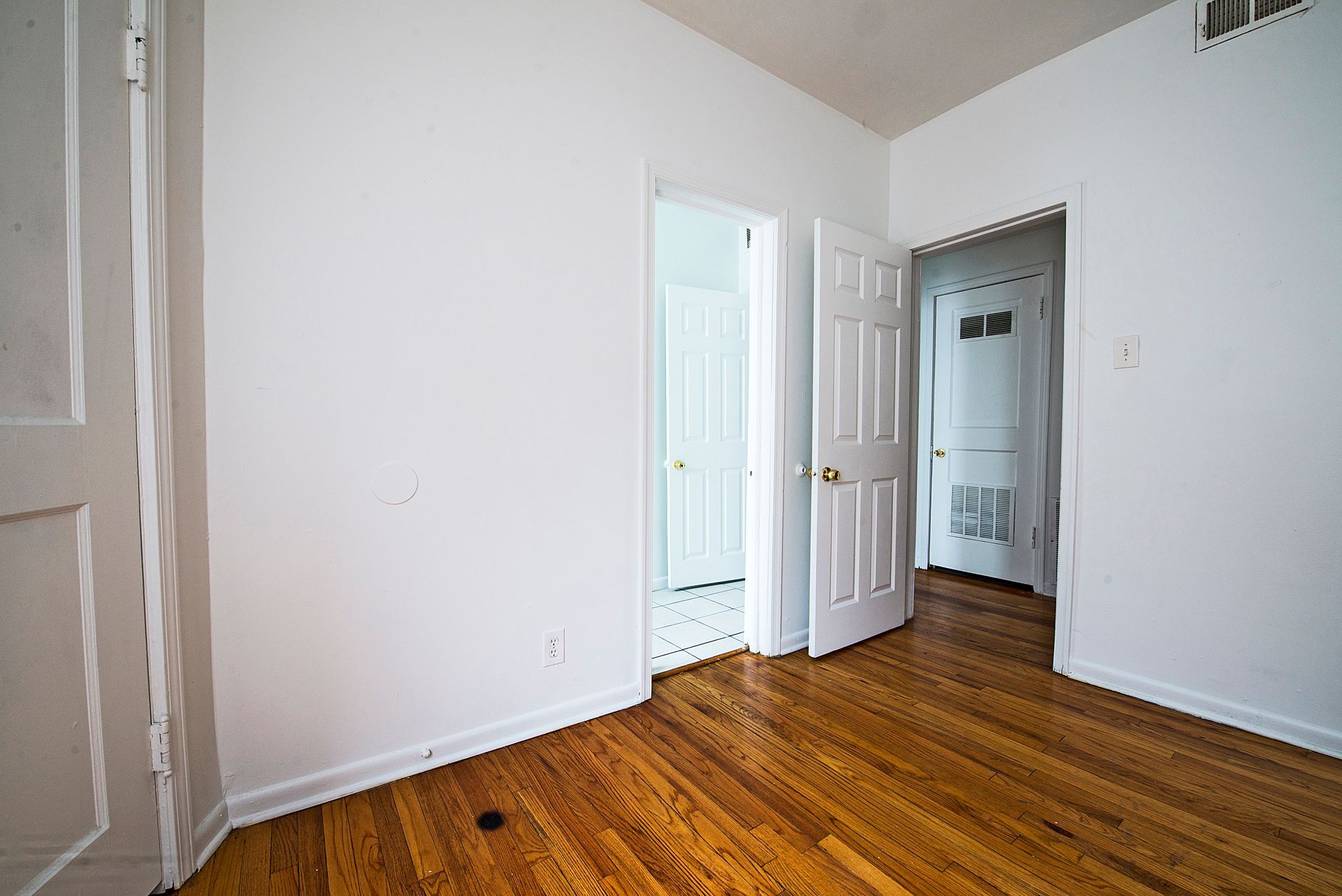 Empty room with wood floors and three white doorways.