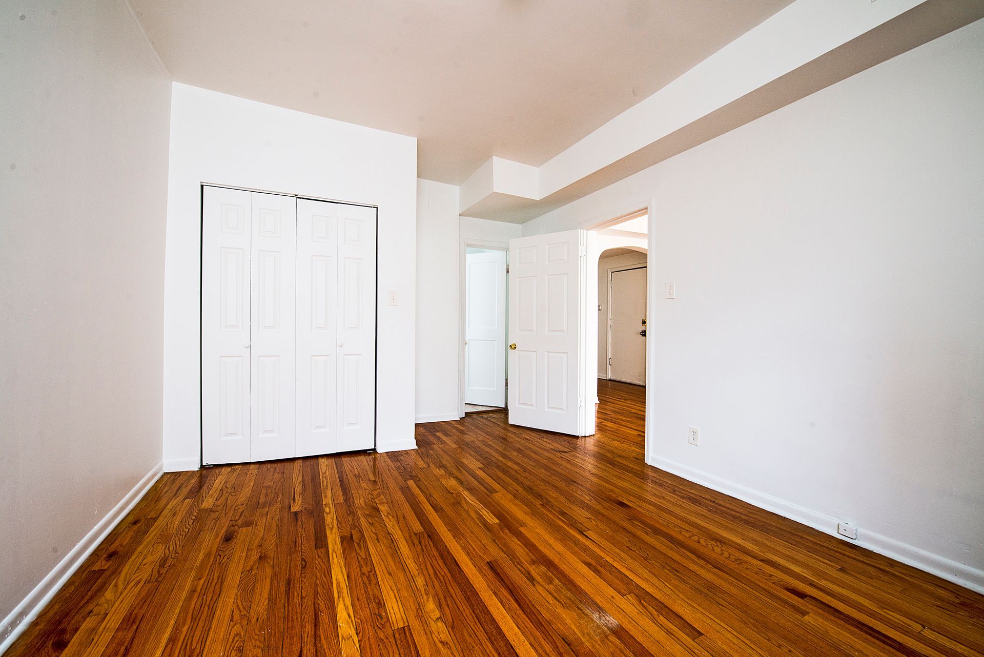 Empty room with hardwood floors, white walls, closet, and doorways.