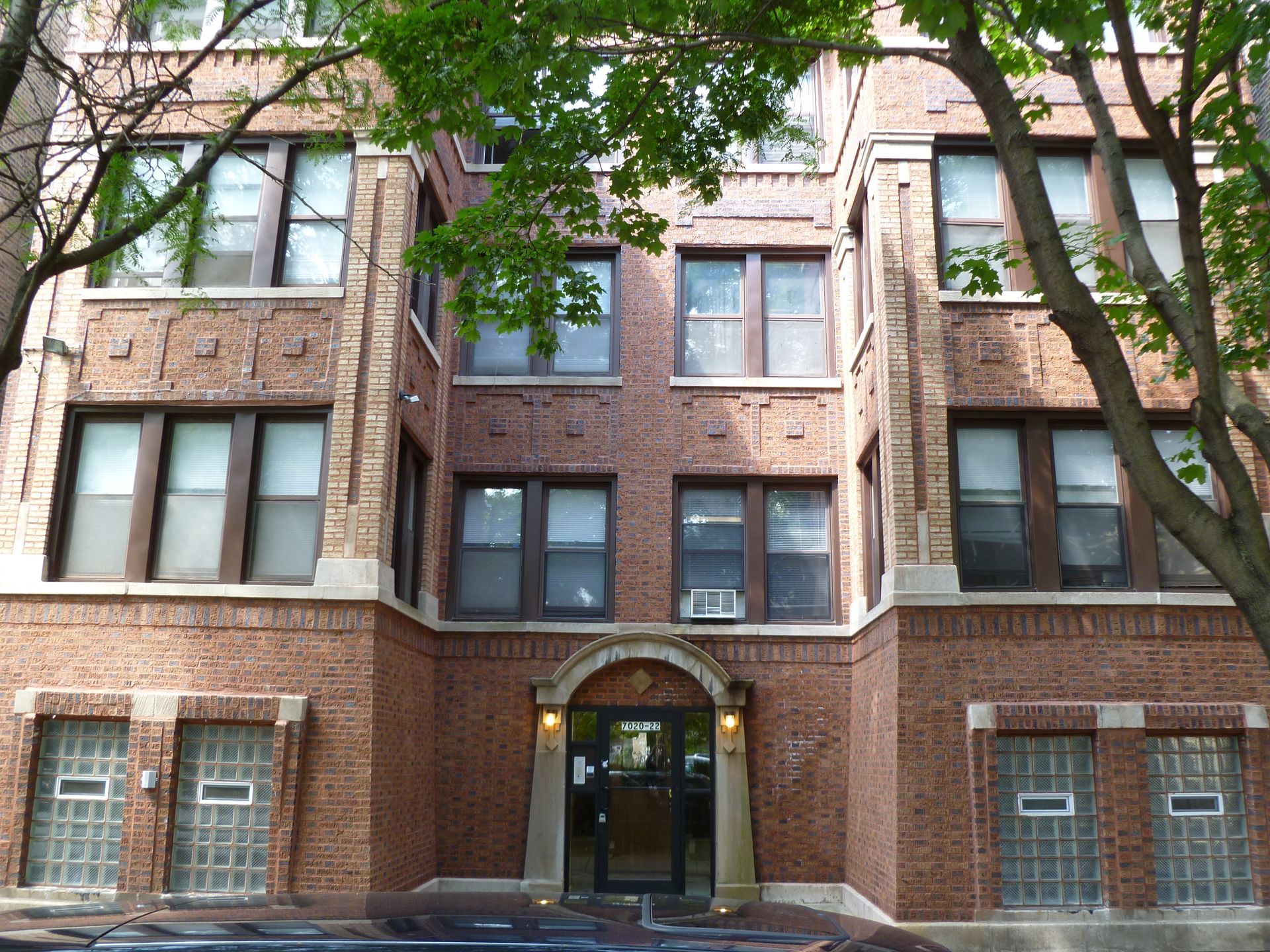 Red brick apartment building with multiple windows and a central arched entrance.