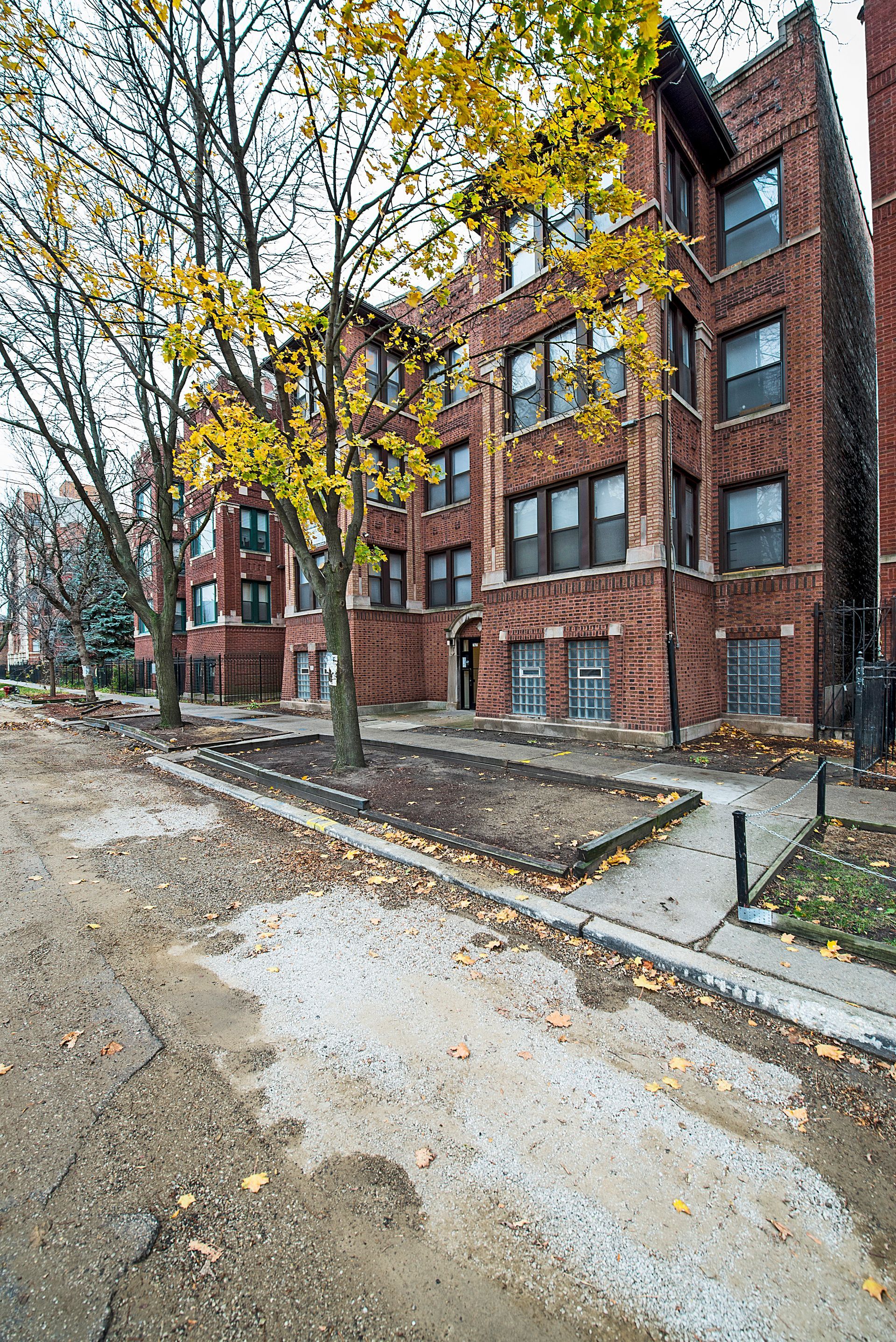 Brick apartment building with fall foliage and a partially paved street.