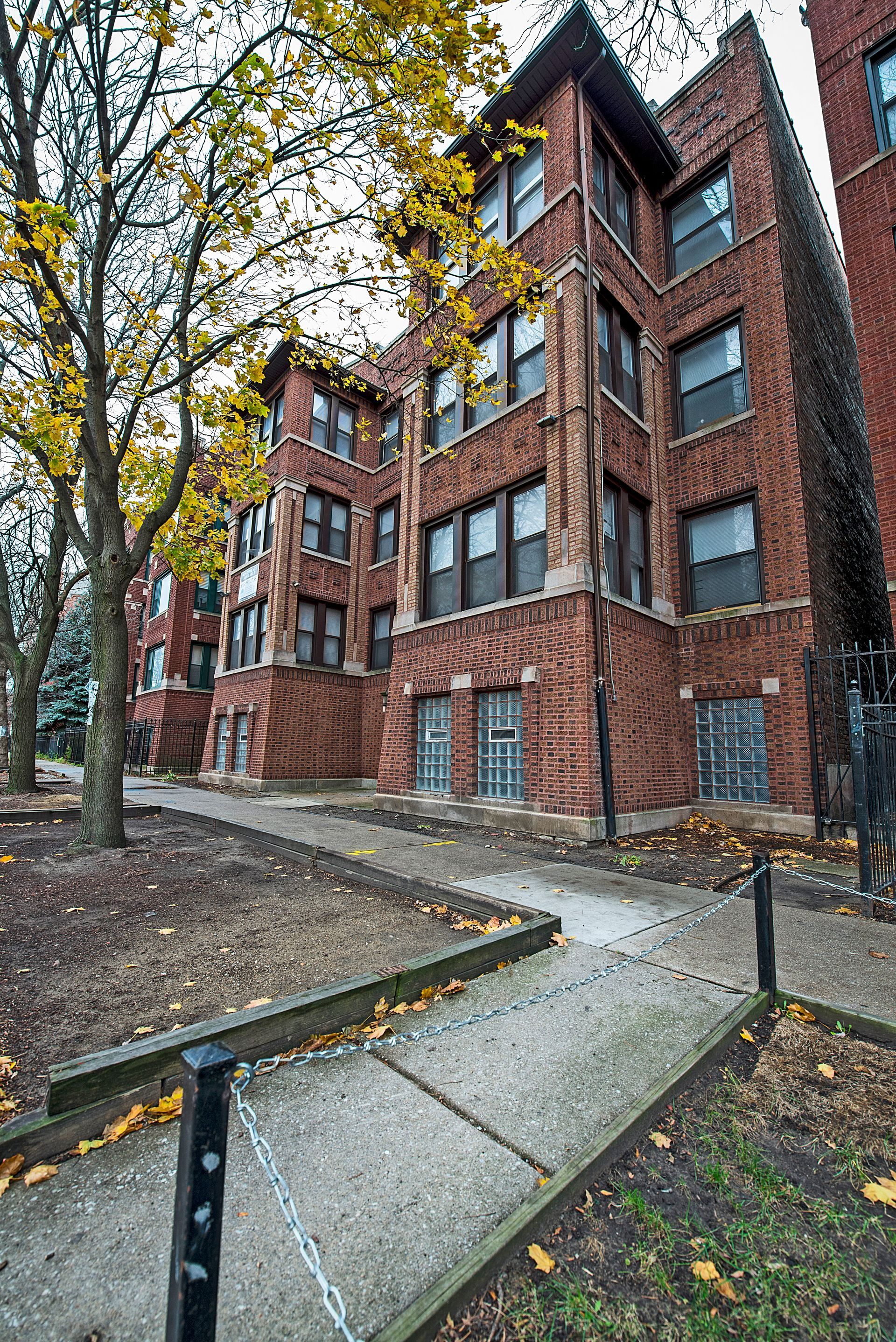 Brick apartment building with walkway and fall foliage.