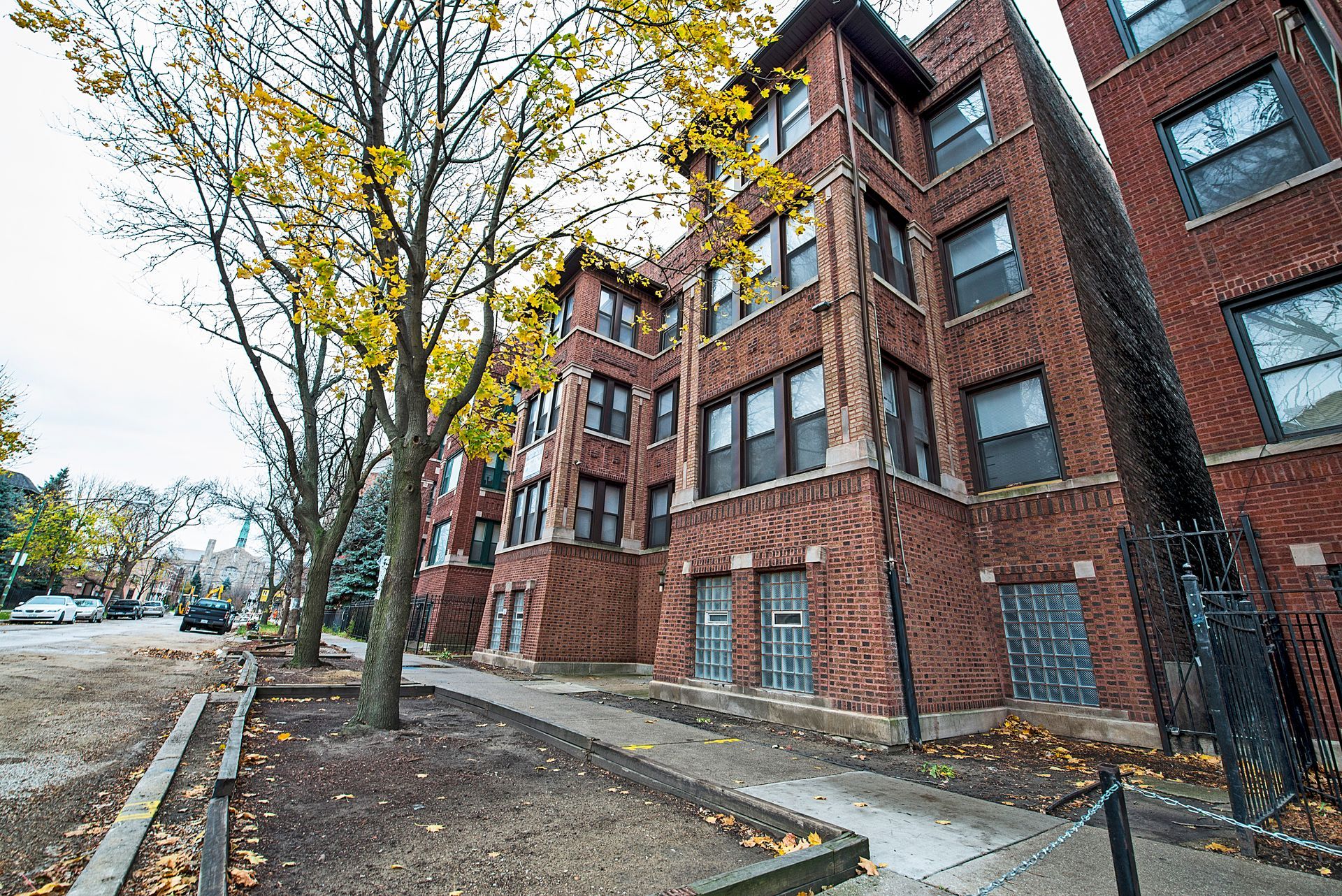 Apartment buildings with brick facade and windows, flanked by trees and a sidewalk.