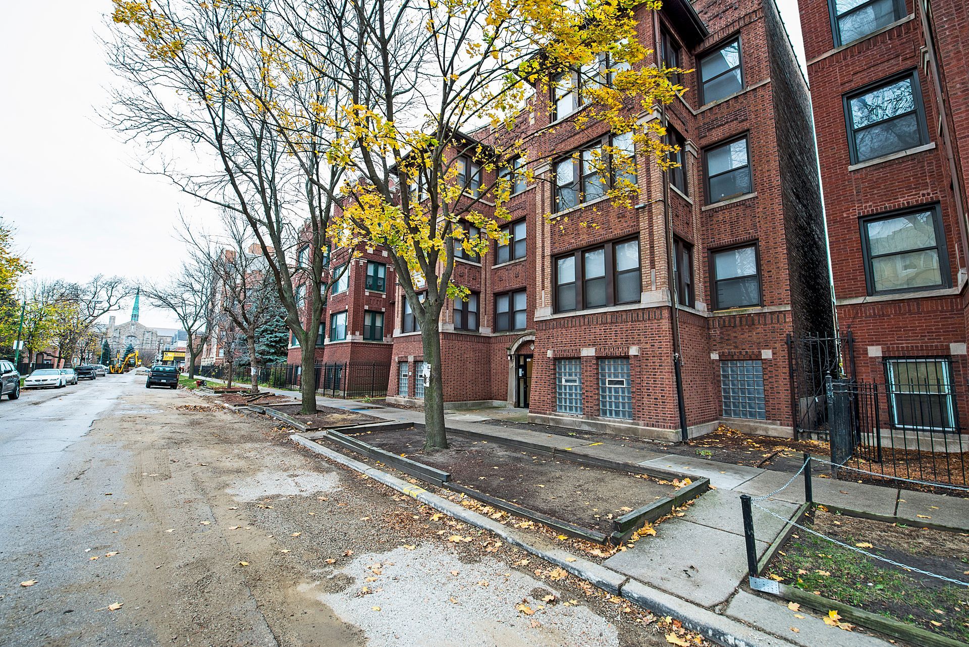Street view of brick apartment buildings with yellow autumn trees and a wet street.