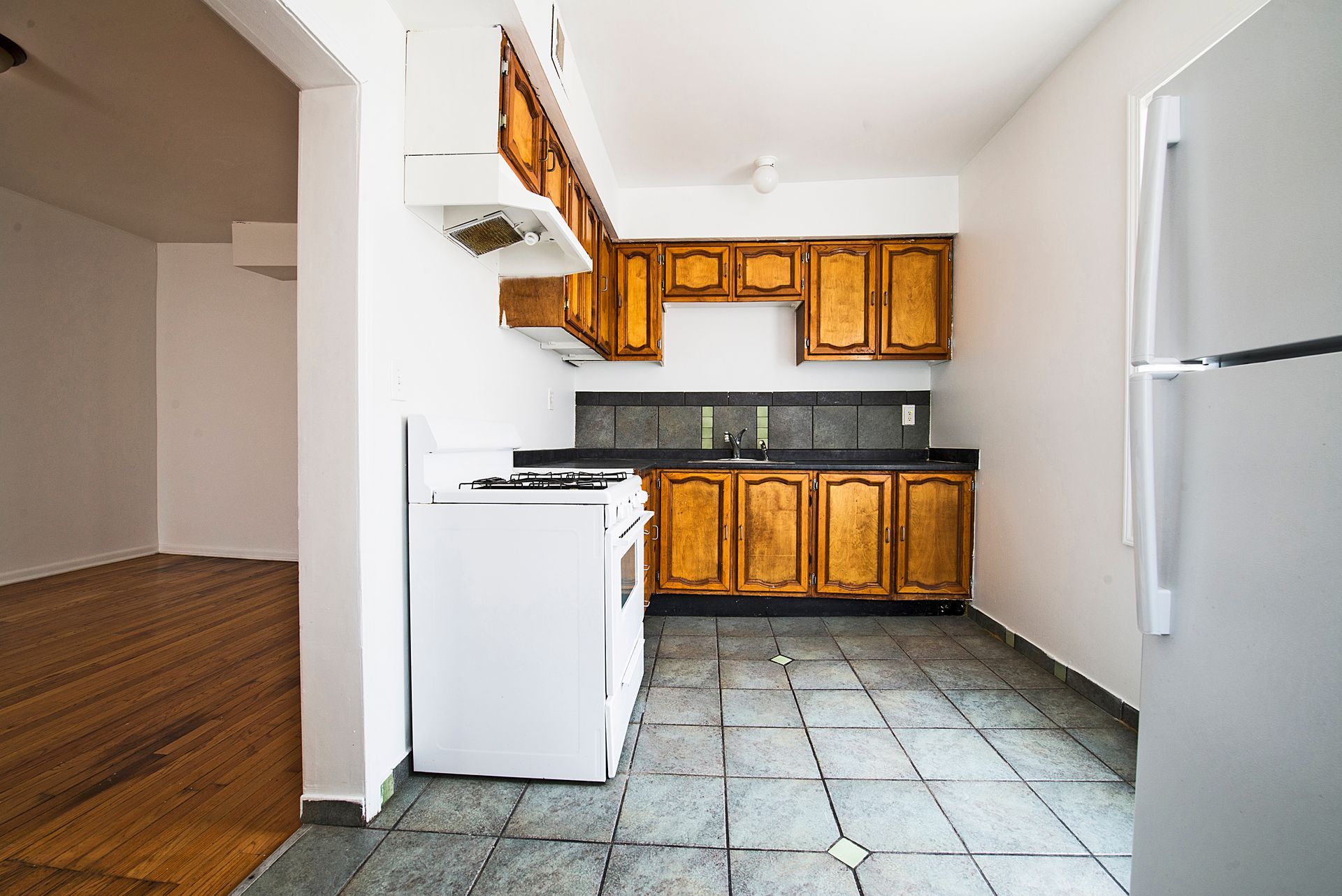 Small kitchen with wood cabinets, white appliances, and gray tiled floor.