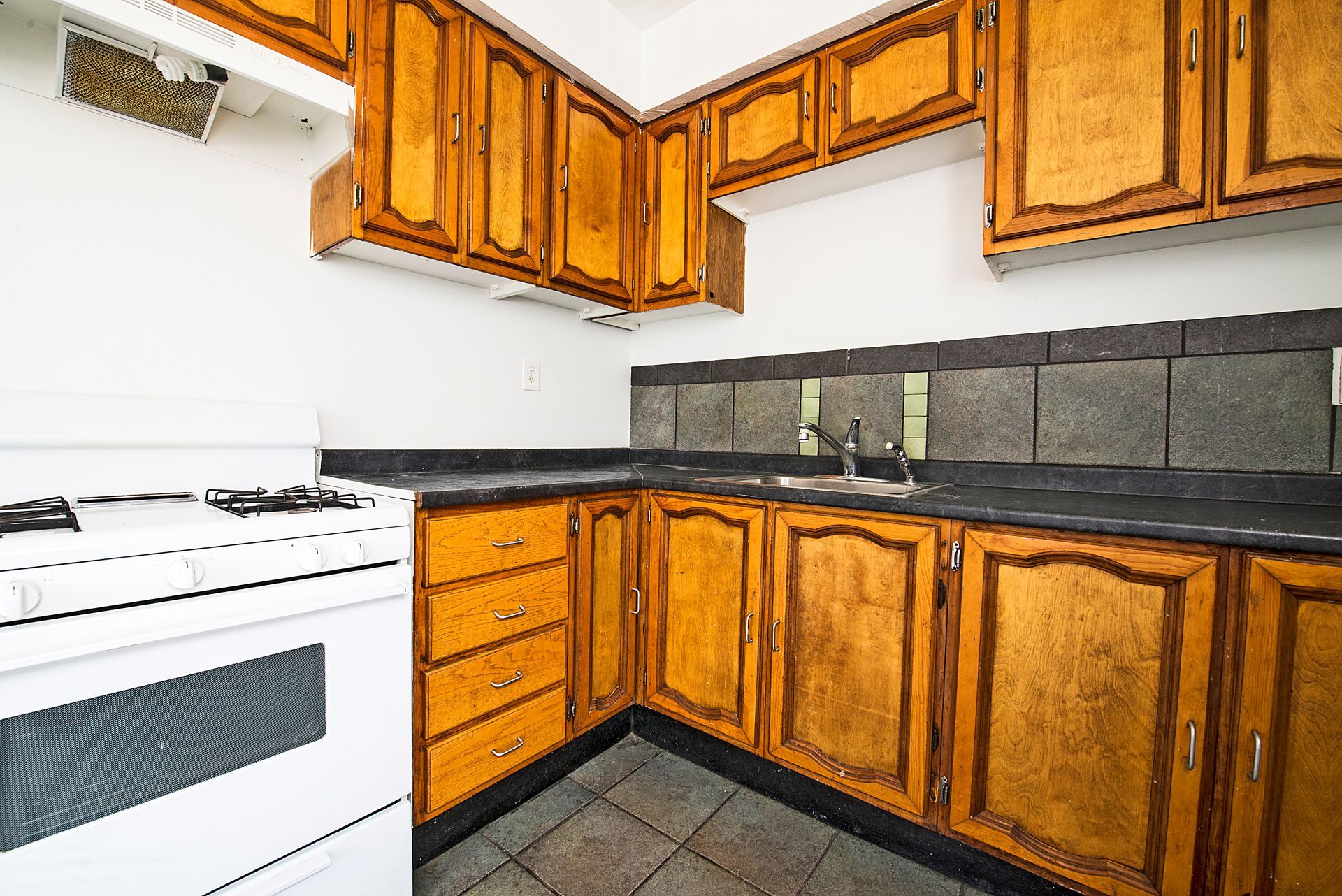 Kitchen with wooden cabinets, white stove, dark countertops, and tile backsplash.