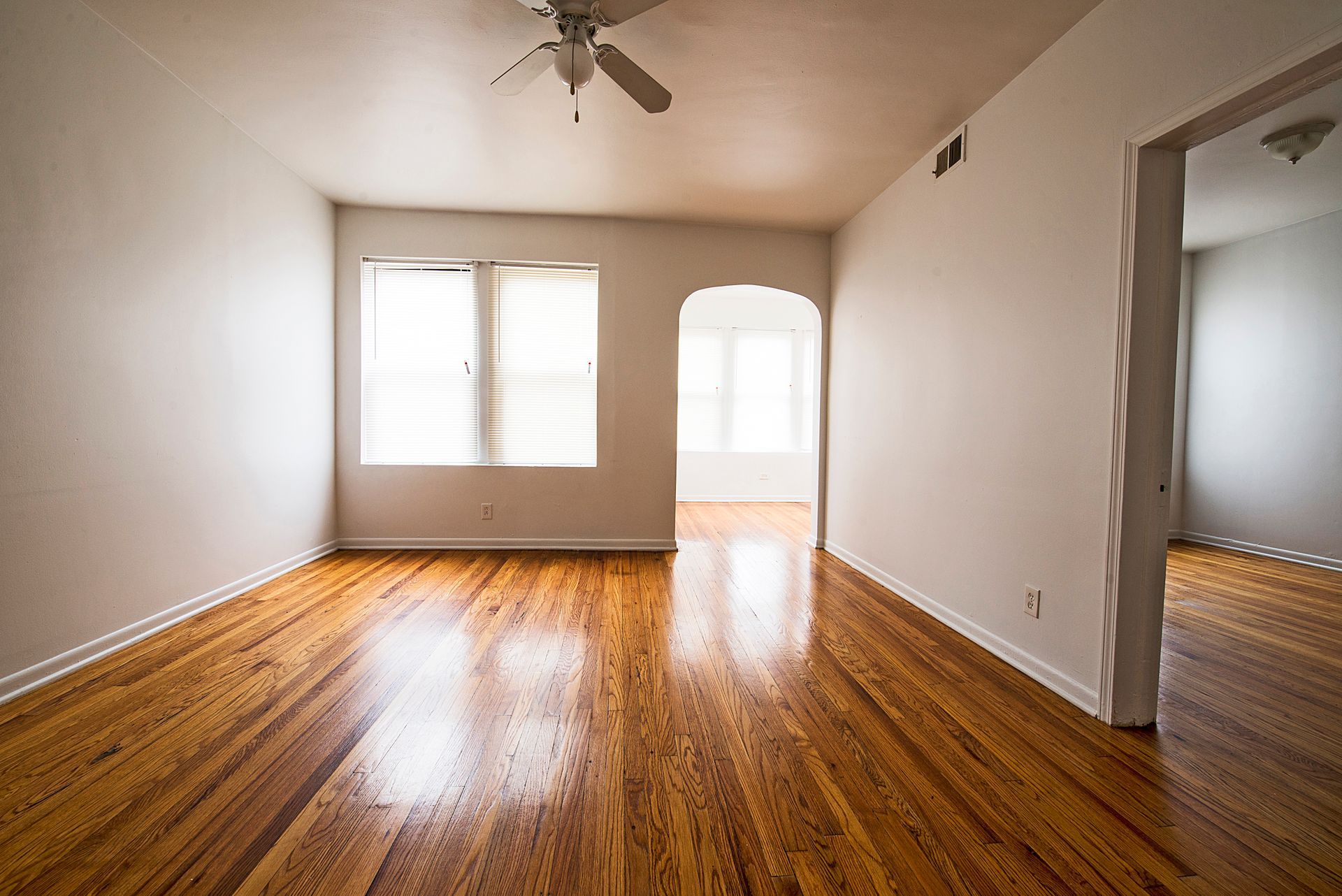 Empty room with hardwood floors, white walls, arched doorway, and a ceiling fan.