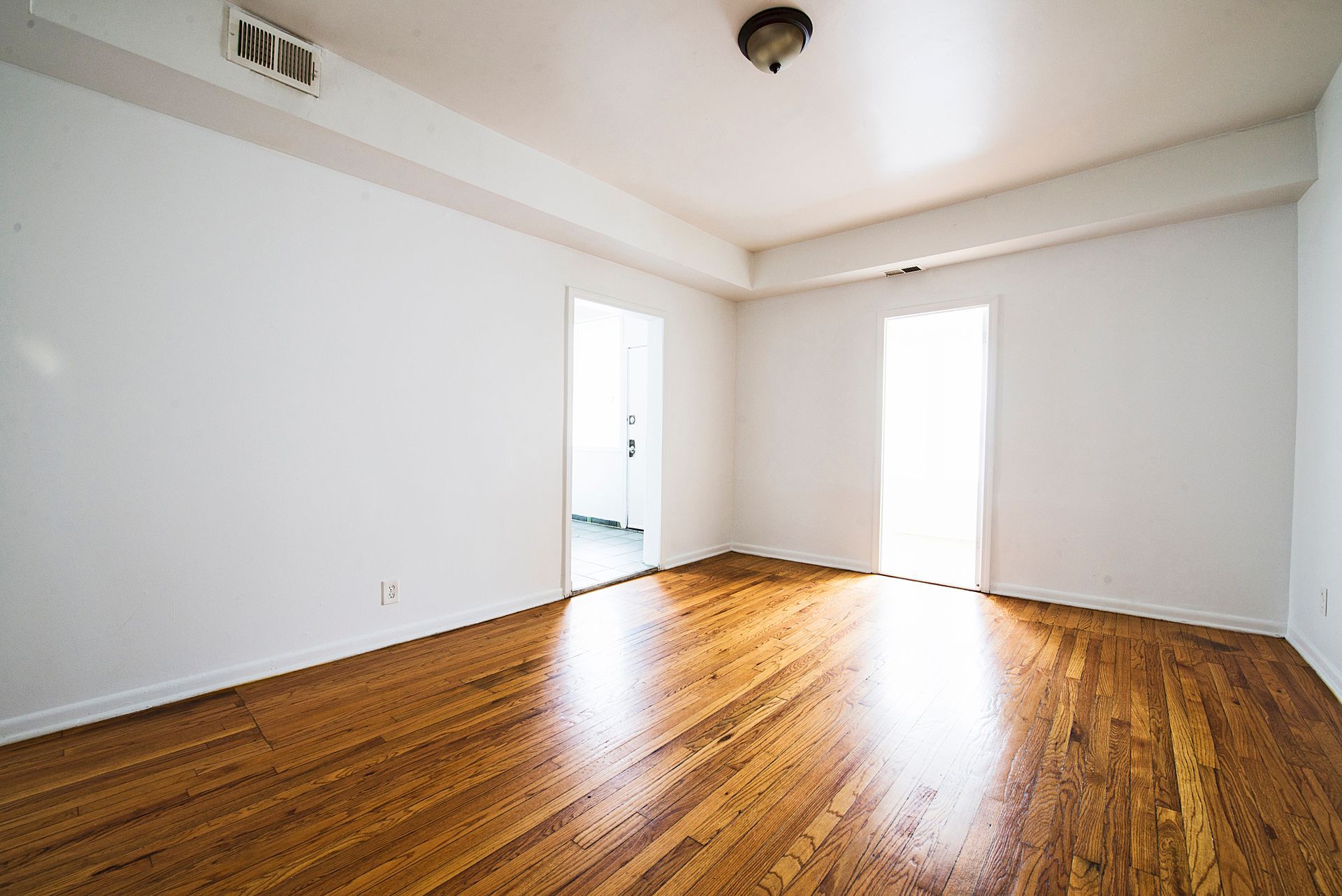 Empty room with hardwood floors, white walls, and bright natural light from a doorway.