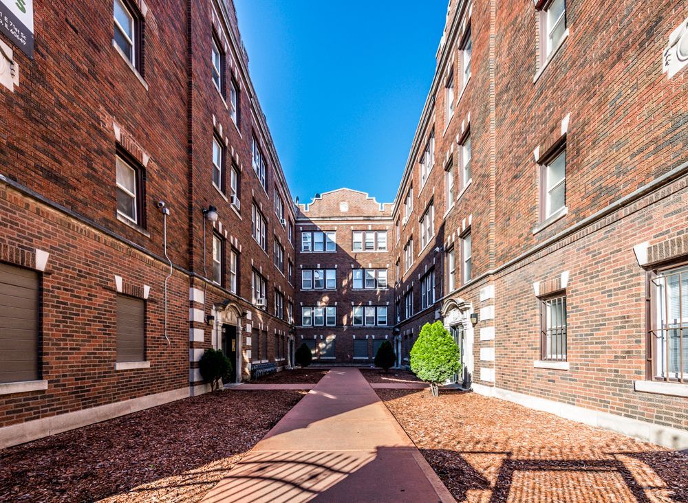 Courtyard between brick apartment buildings, brown gravel, clear blue sky.