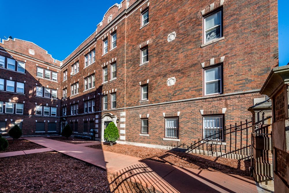 Red brick apartment building with courtyard and wrought iron fence.