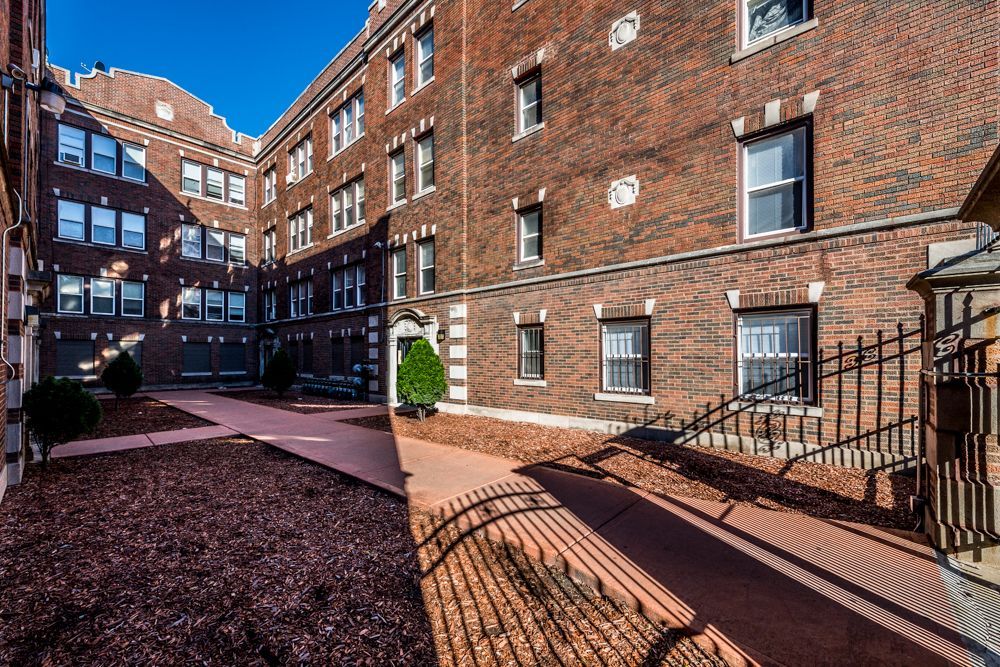 Brick apartment building courtyard with paved walkways and landscaping.