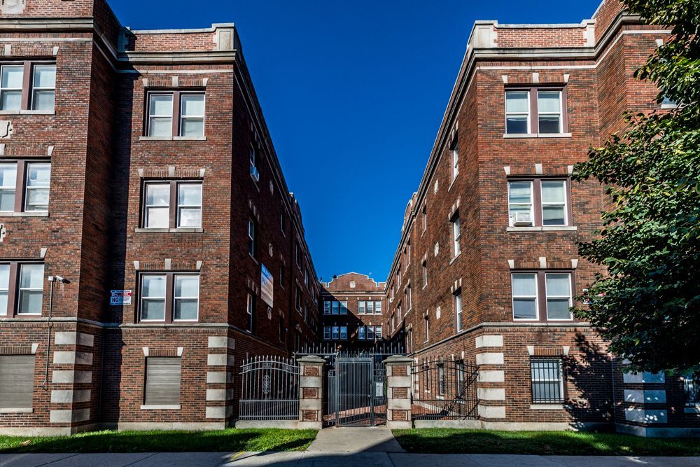 Two brick apartment buildings with white trim, facing each other. Blue sky background.