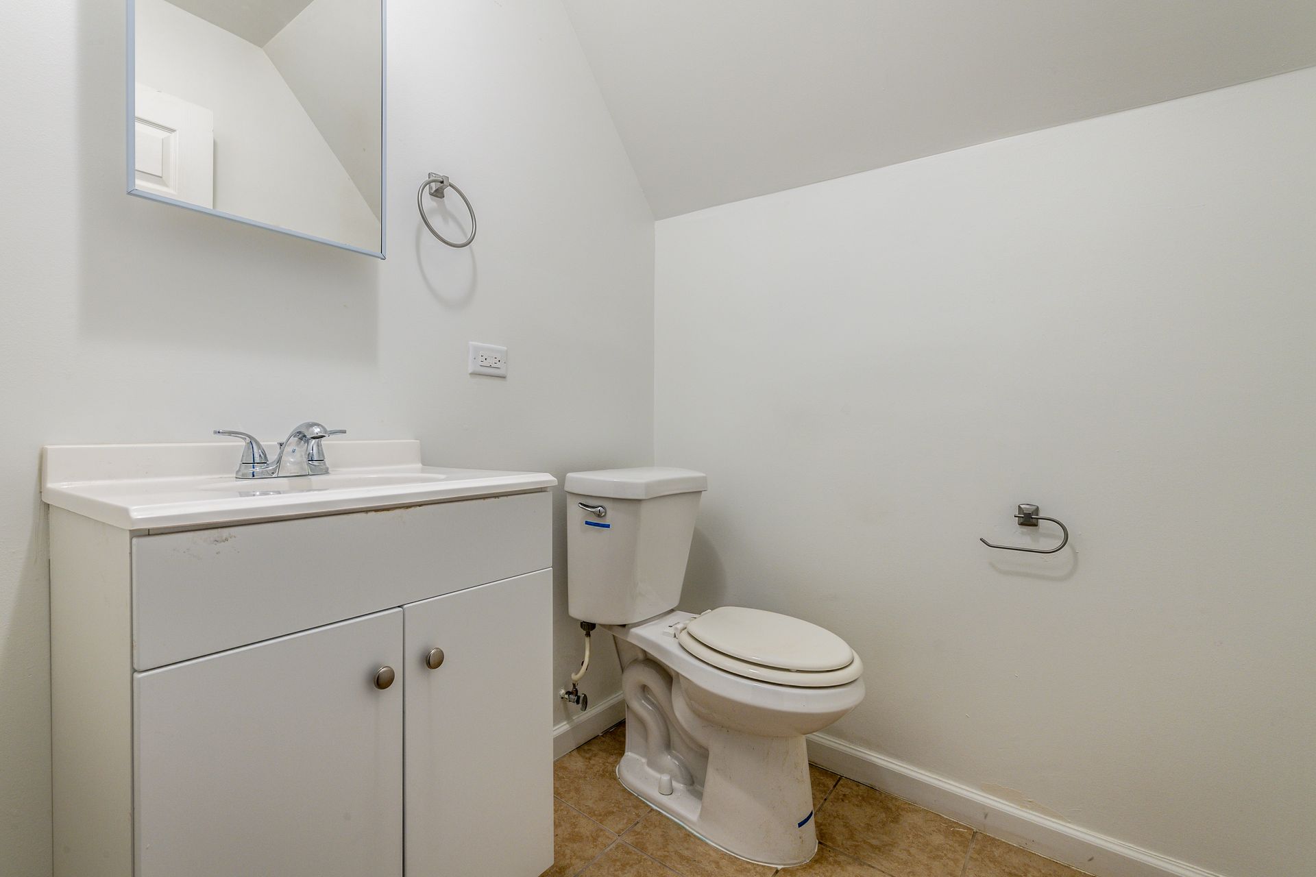 White bathroom with a sink, toilet, and mirror. Tan flooring.