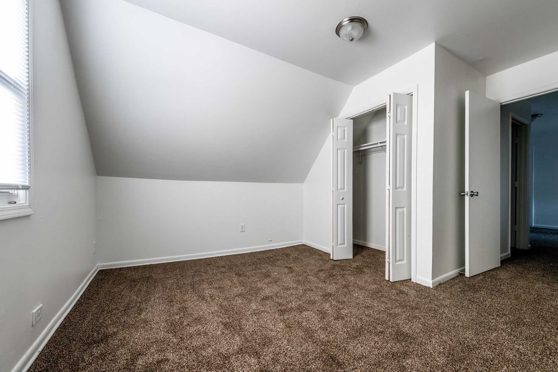 Empty bedroom with angled ceiling, closet, and brown carpet.