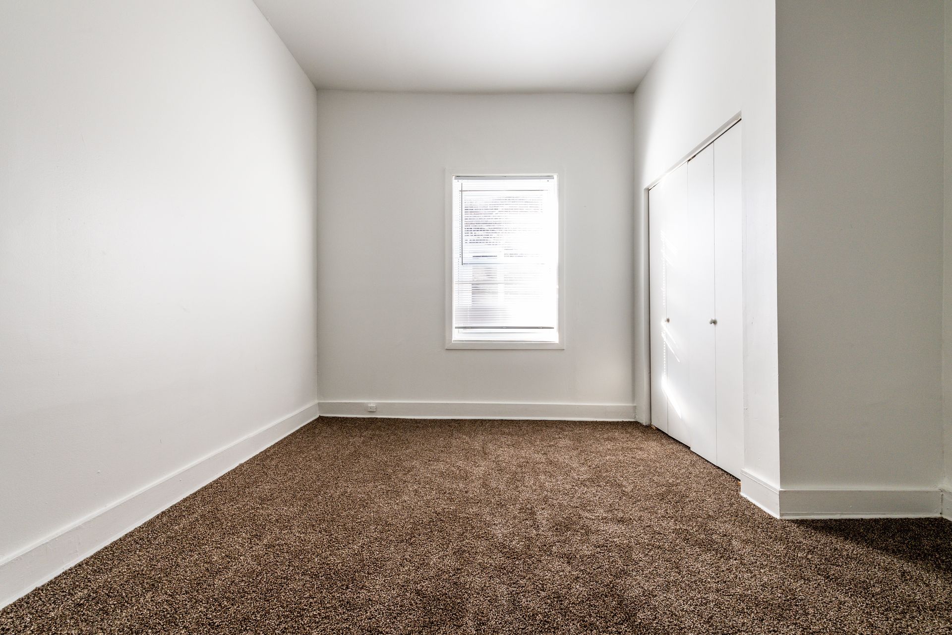 Empty room with brown carpet, white walls, small window, and closet.