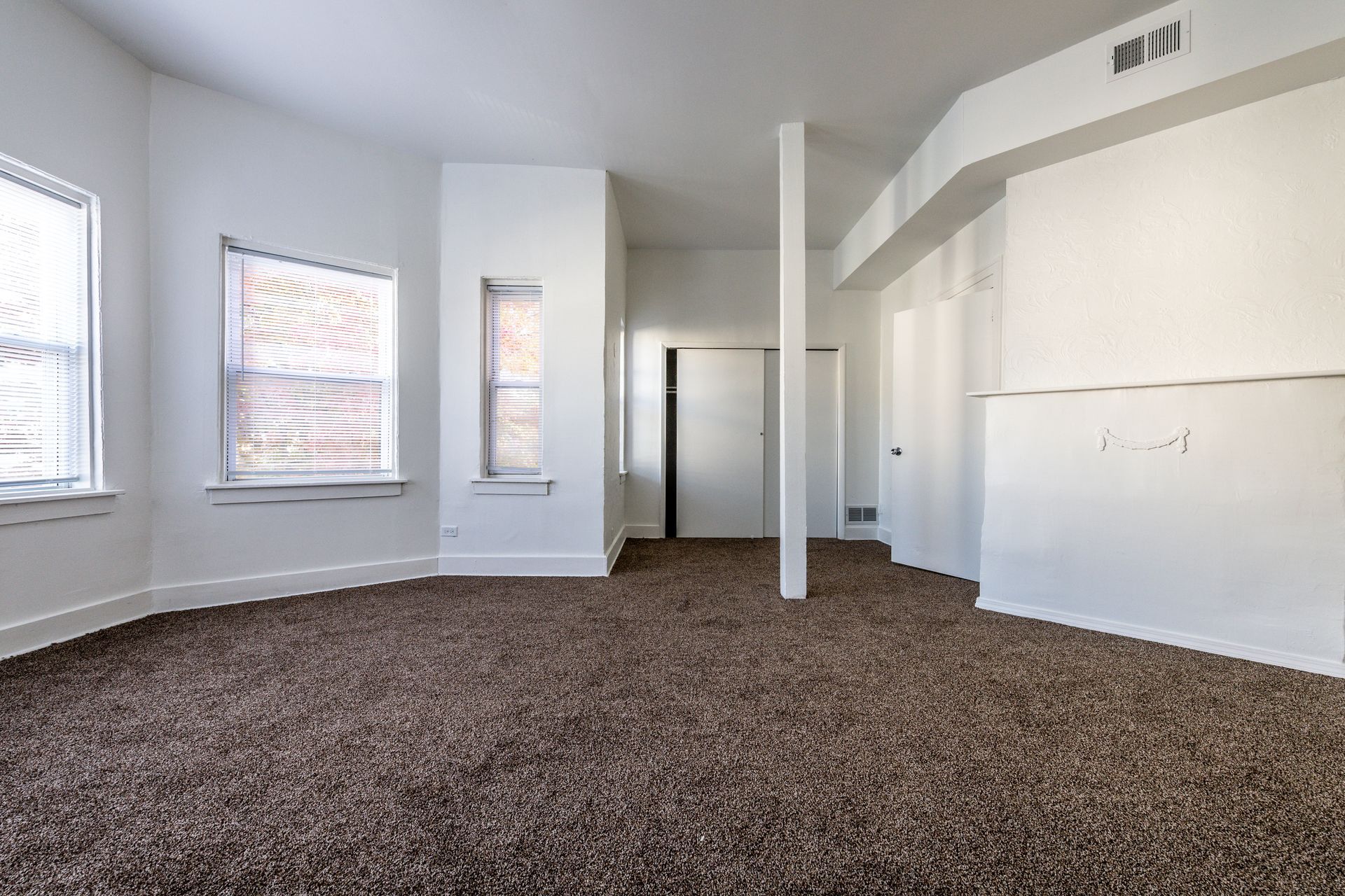 Empty room with brown carpet, white walls, two windows, and a closet.
