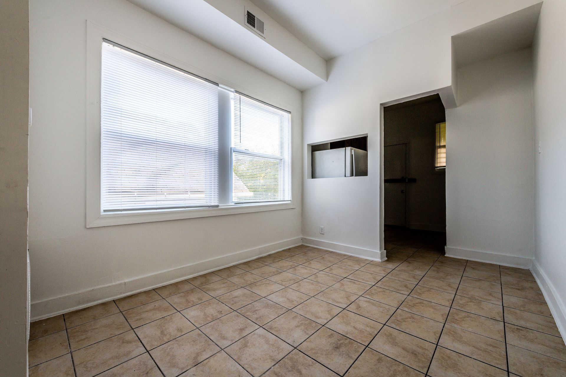 Empty room with tiled floor, window, and doorway. White walls and a recessed microwave.