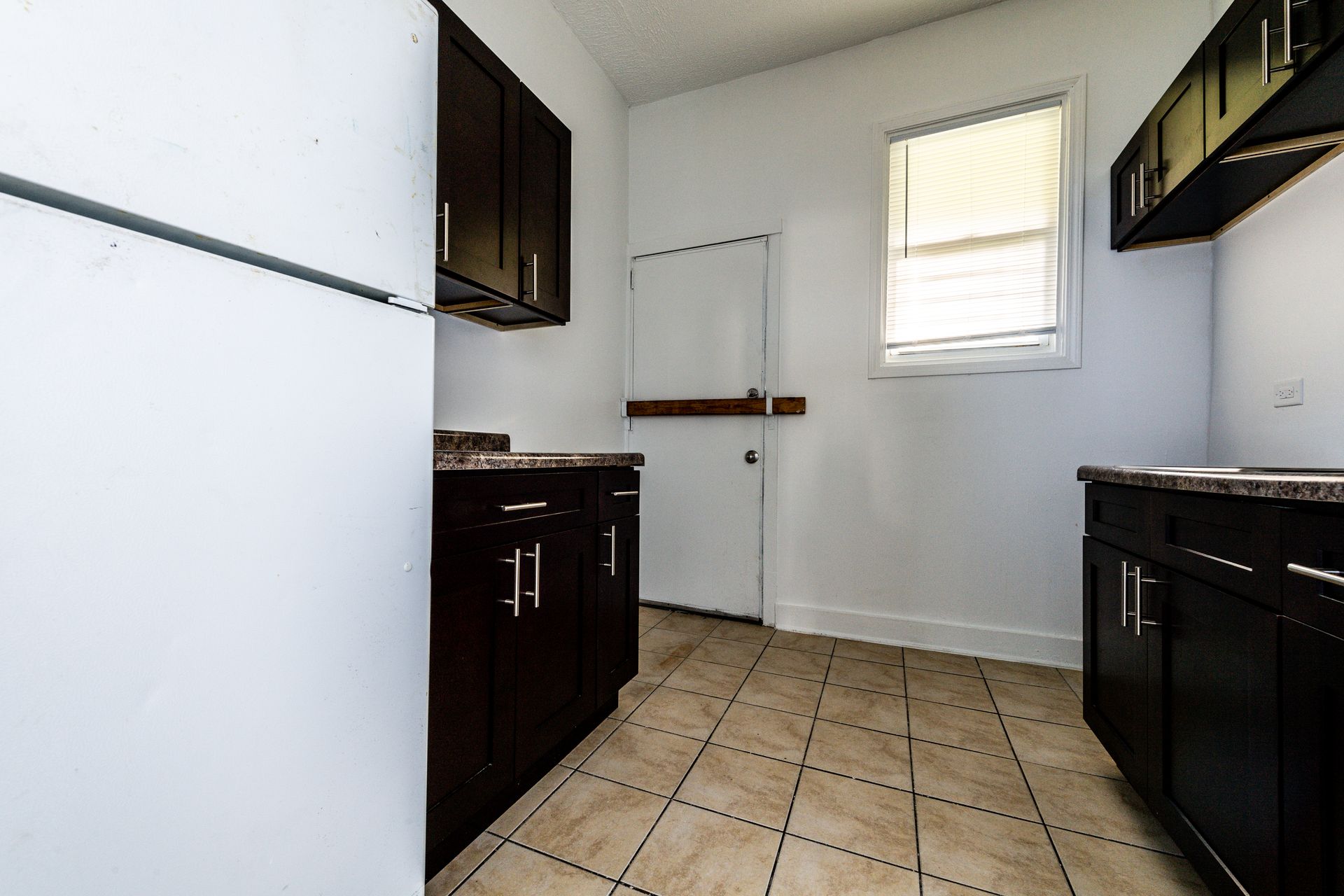 Empty kitchen with dark brown cabinets, white appliances, and a window.