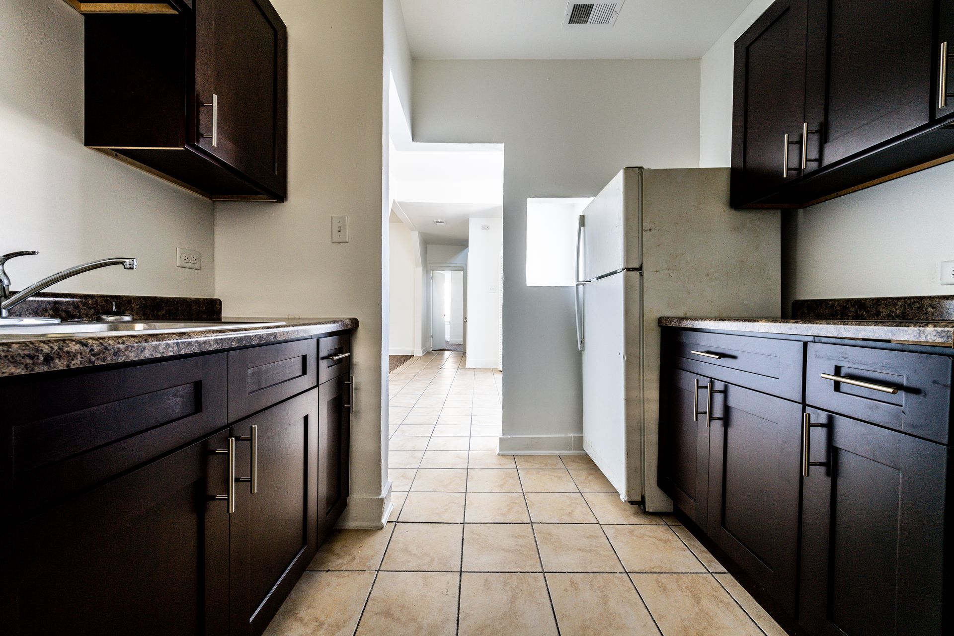 Kitchen with dark brown cabinets, a white refrigerator, and a view into a hallway.