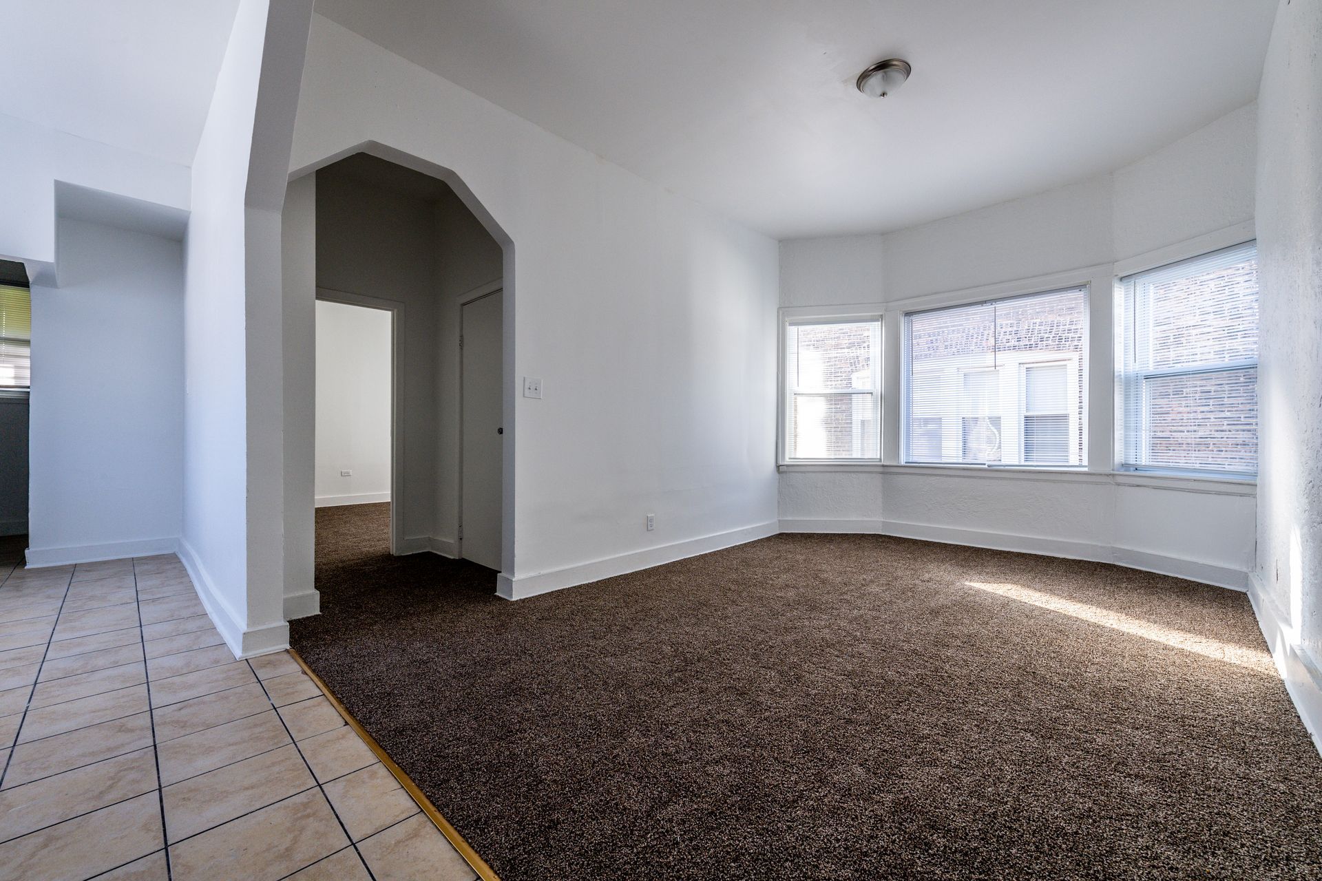 Empty room with brown carpet, white walls, and a bay window.