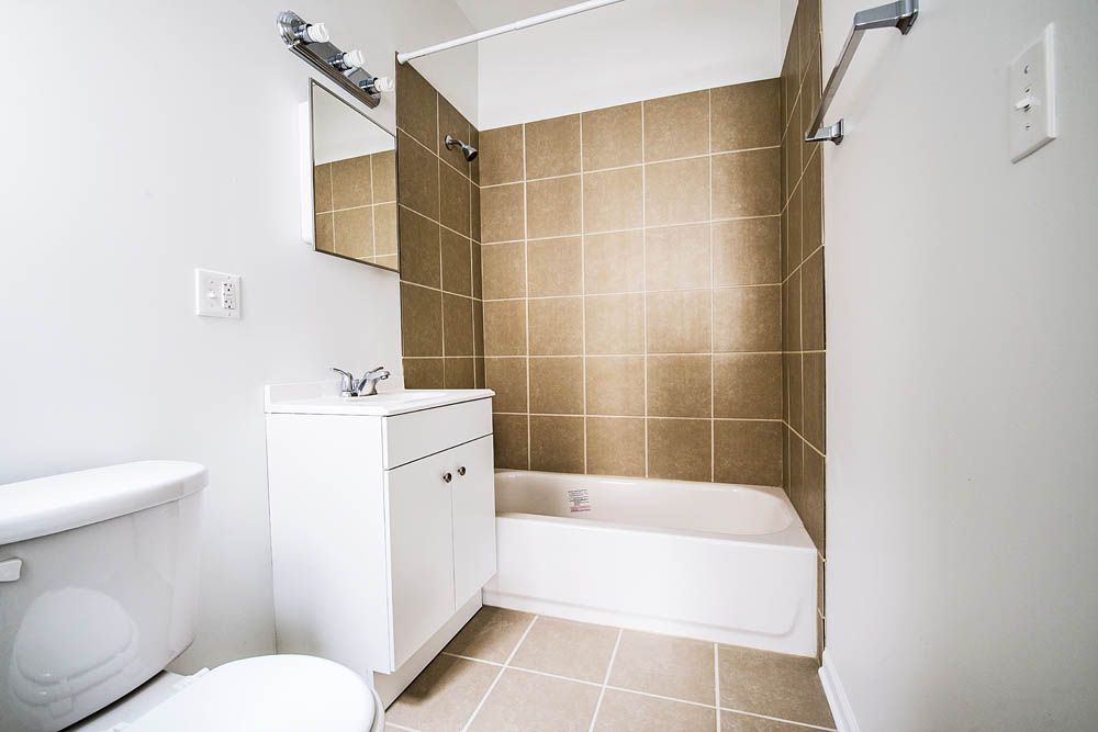 Small bathroom with a white toilet, sink cabinet, and bathtub. Brown tile surrounds the tub.