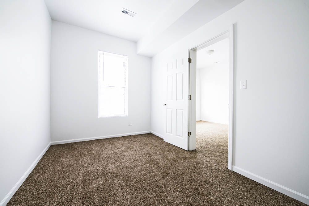 Empty white room with brown carpet, doorway, and a window.