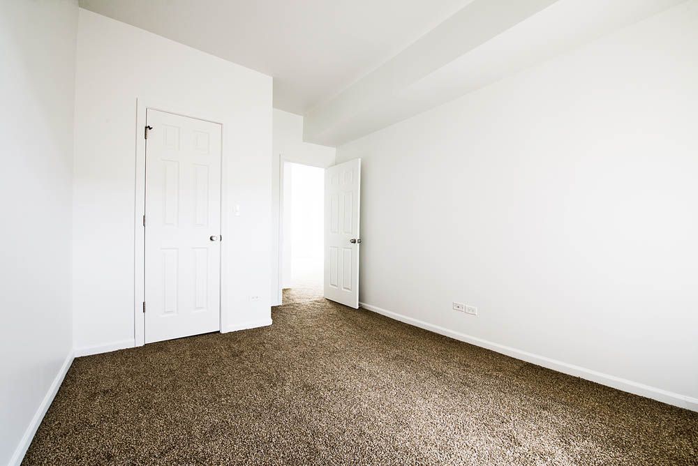 Empty room with white walls, beige carpet, and two white doors.