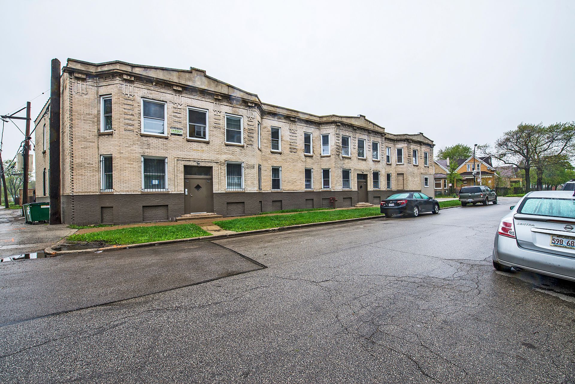 Row of weathered buildings on a rainy street, parked cars, overcast sky.