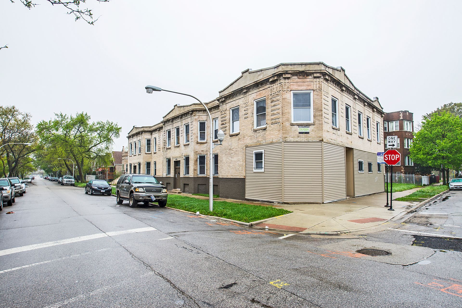 Corner building with light-colored facade, street and parked cars, overcast sky.