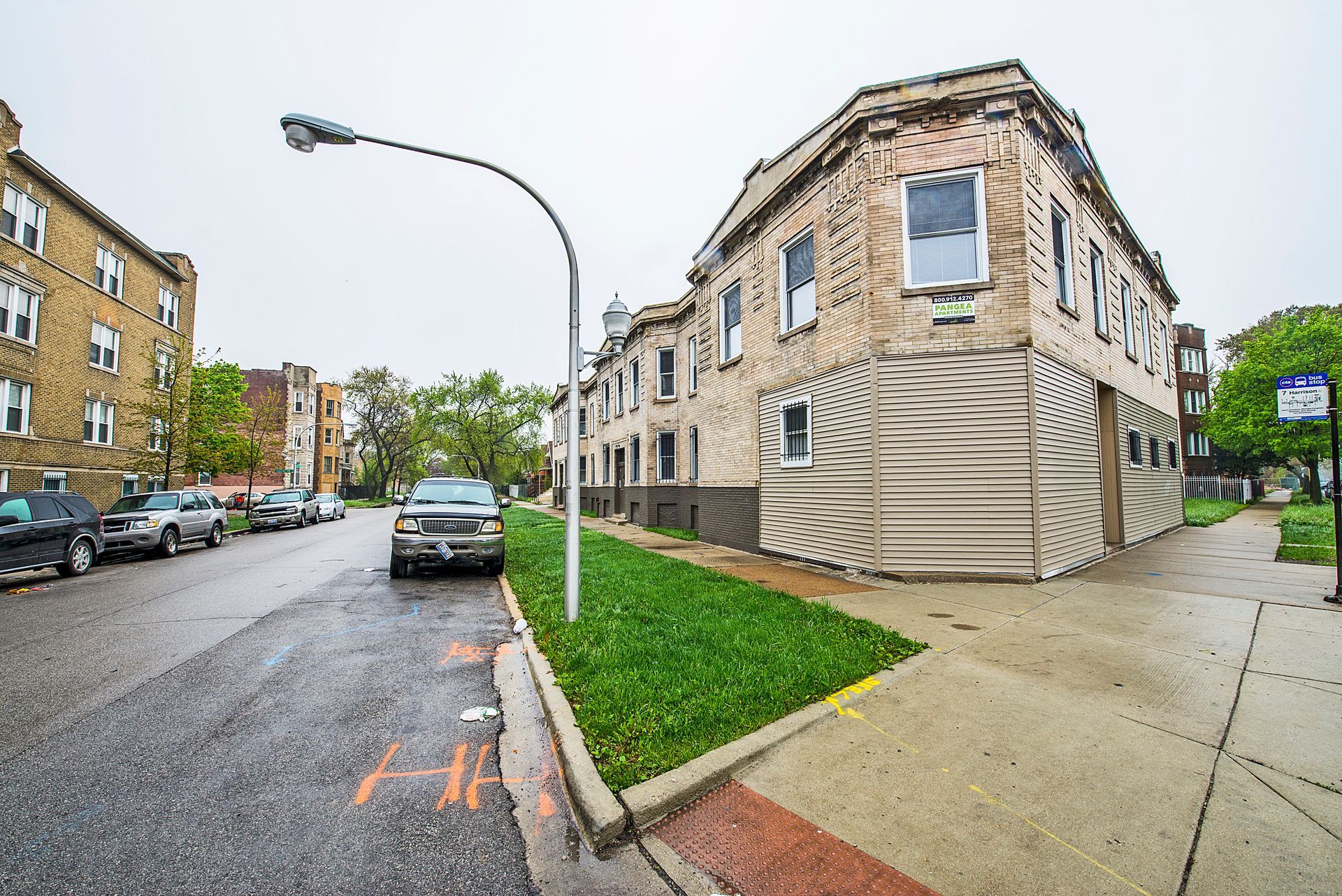 A street scene with buildings and a parked car. Green grass borders a building with an unusual textured facade.
