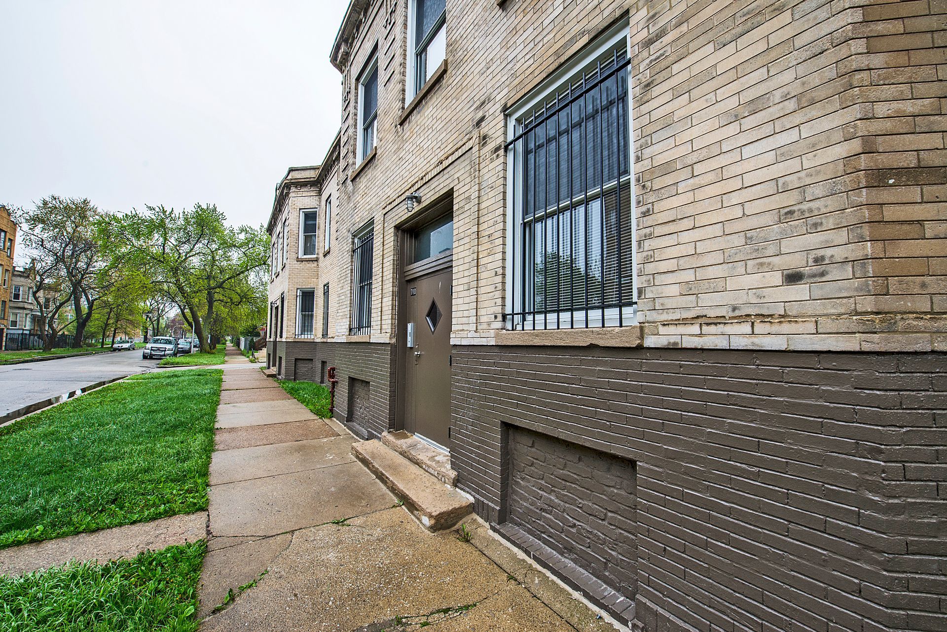 Brick building with barred window, sidewalk, green grass, and street. Overcast day.