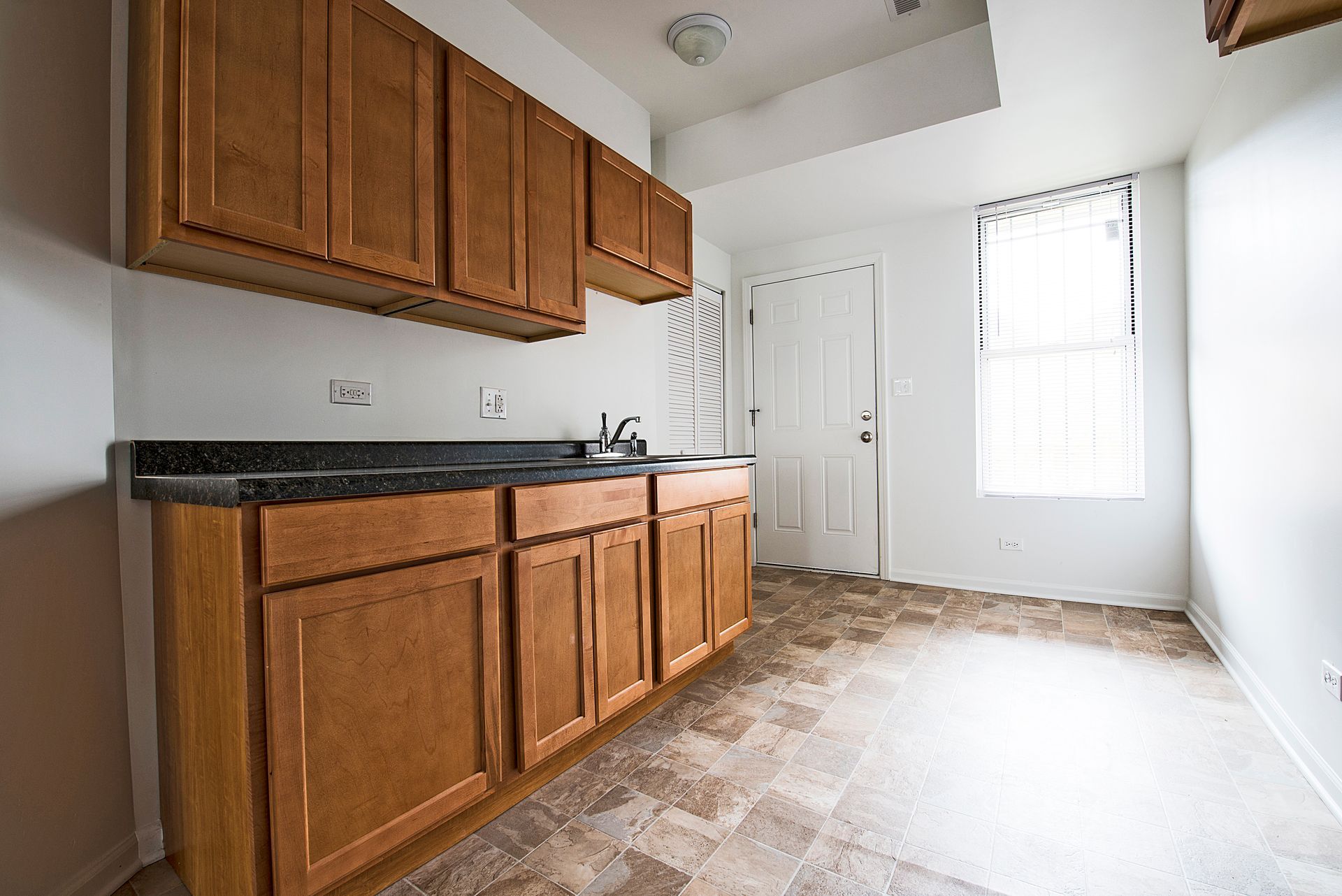Kitchen with brown cabinets, dark countertop, and window with blinds.