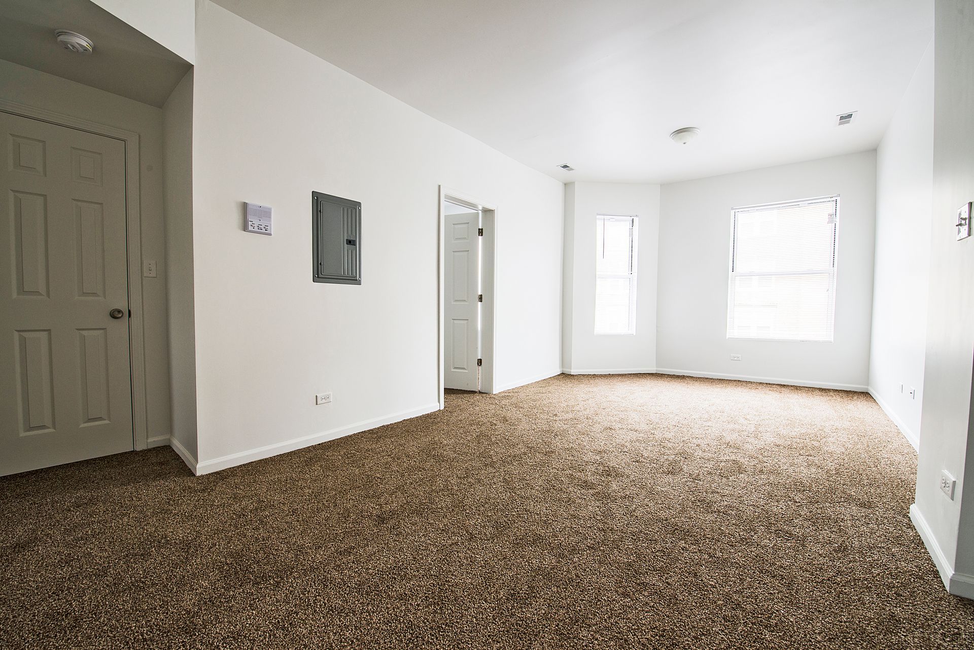 Empty room with brown carpet, white walls, and two doors. One window with blinds.
