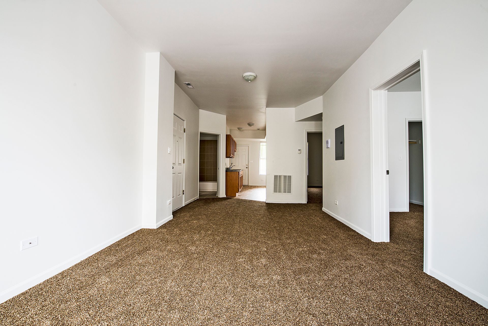Empty room with brown carpet, white walls, and doorways leading to other rooms.