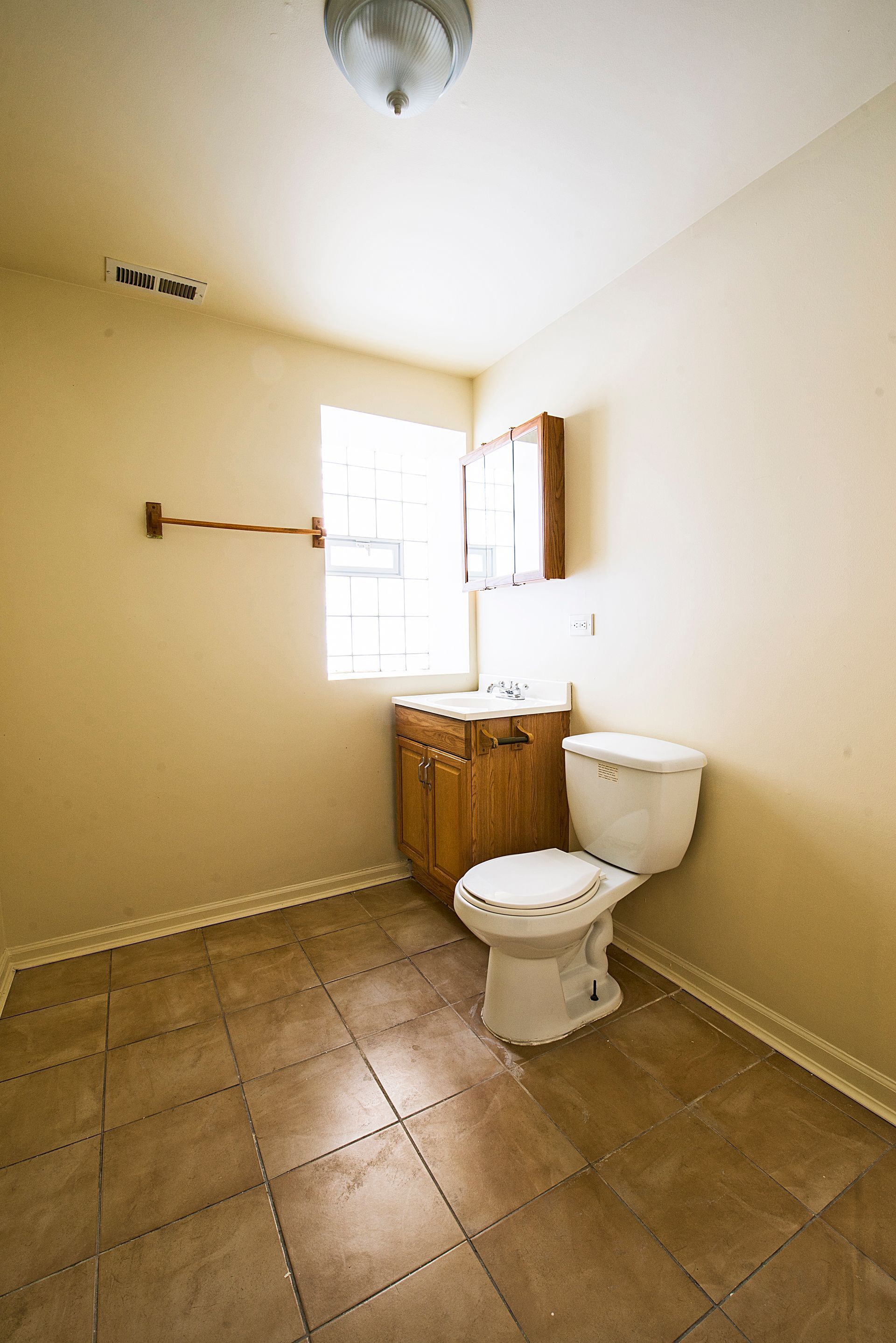 Bathroom with toilet, vanity, and window; neutral-toned walls and floor.