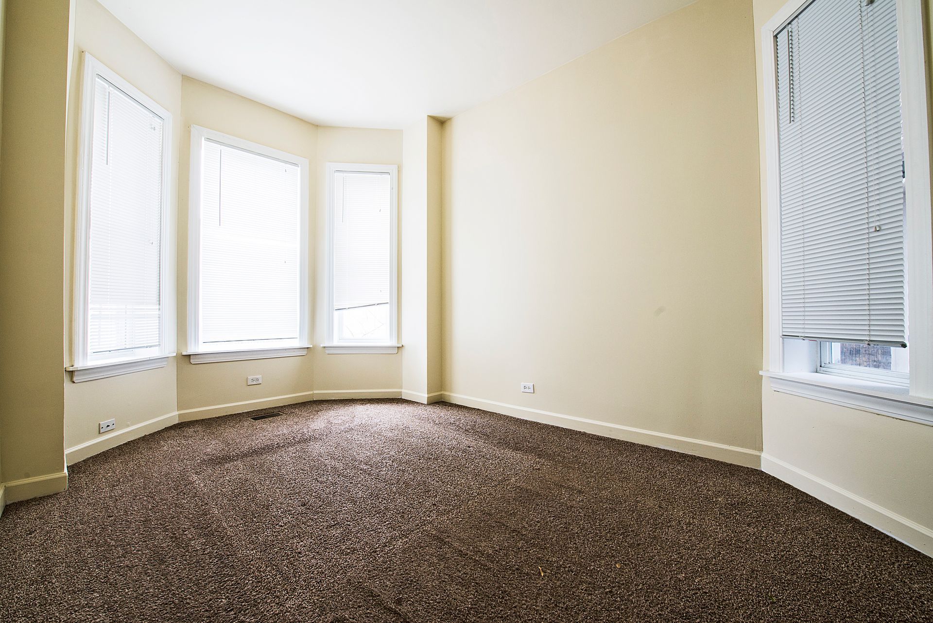 Empty room with carpet and windows; beige walls, brown carpet.