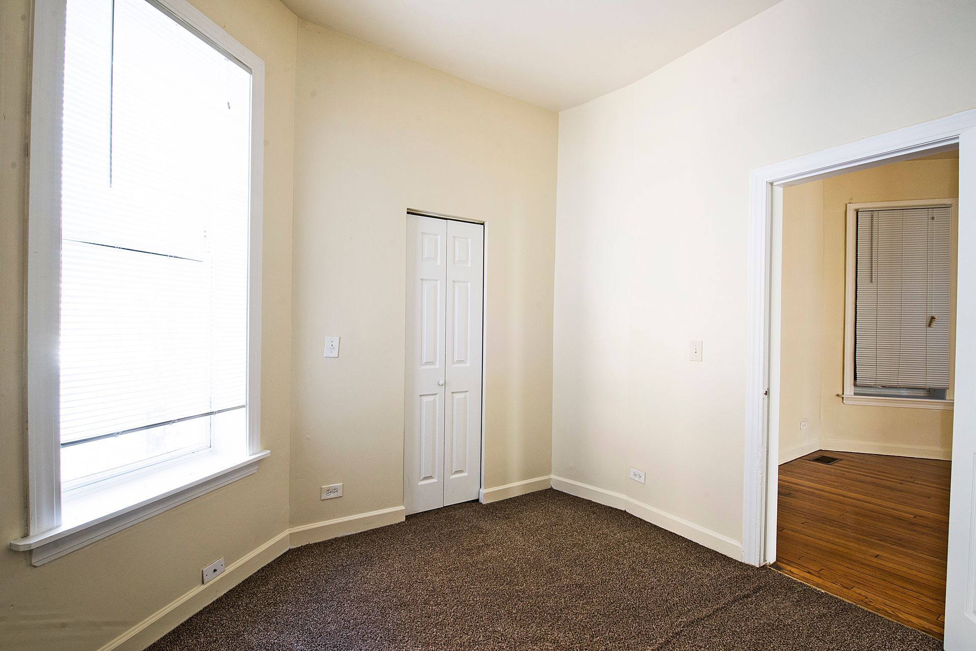 Empty room with a window, doorway, and closet. Brown carpet and light walls.