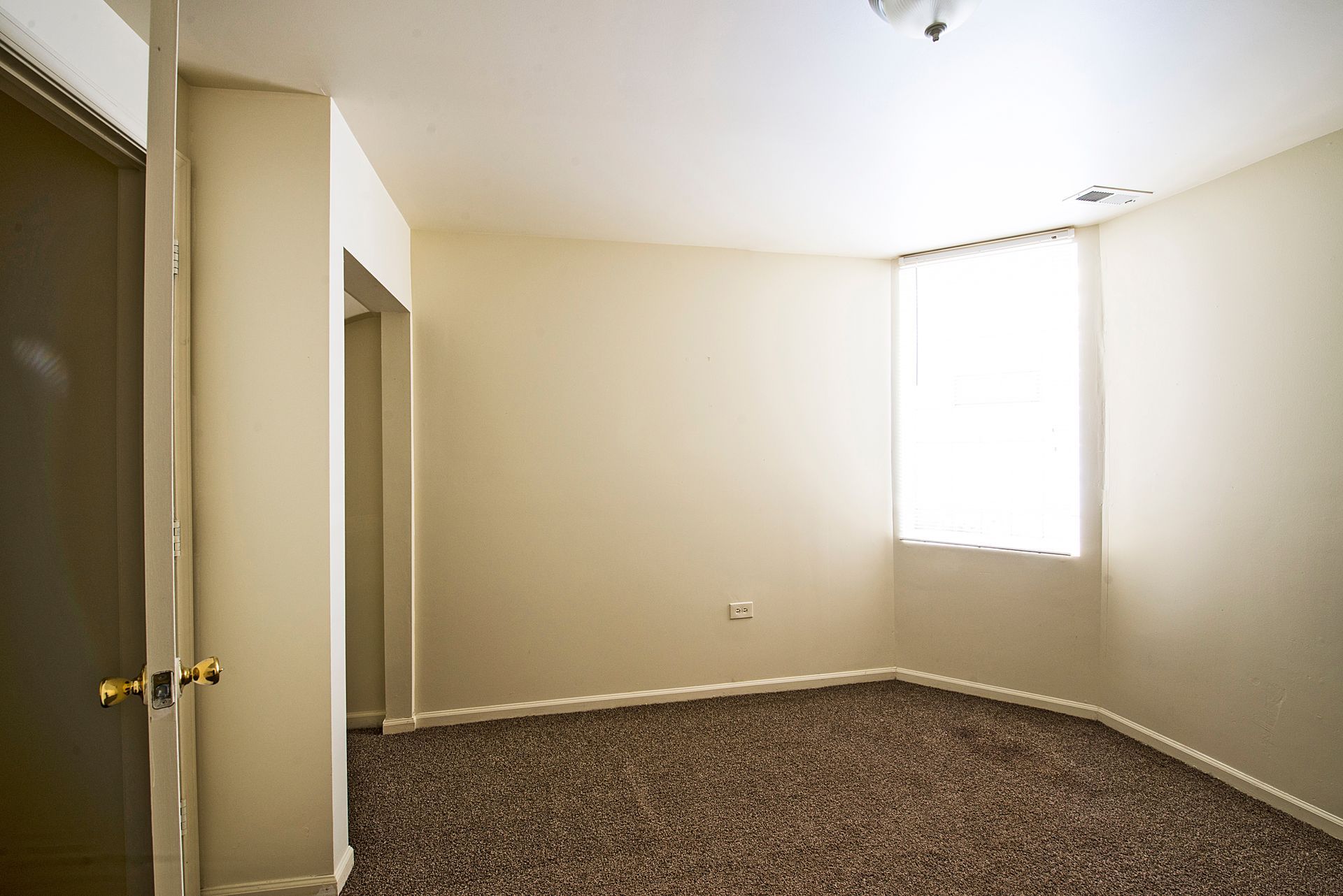 Empty room with beige walls, brown carpet, and a window with natural light.