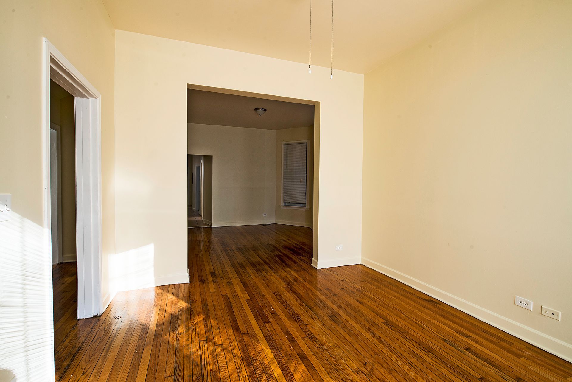Empty room with hardwood floors, doorways, and beige walls.