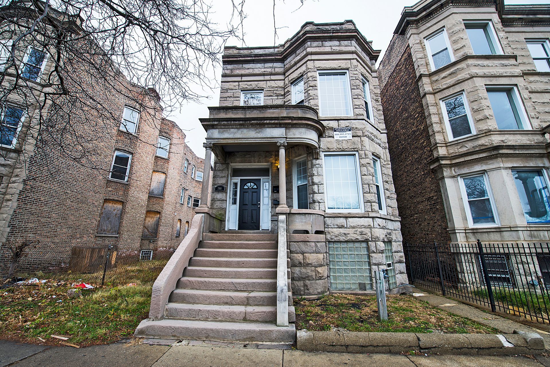 Stone multi-story apartment building with front stairs and a small porch.